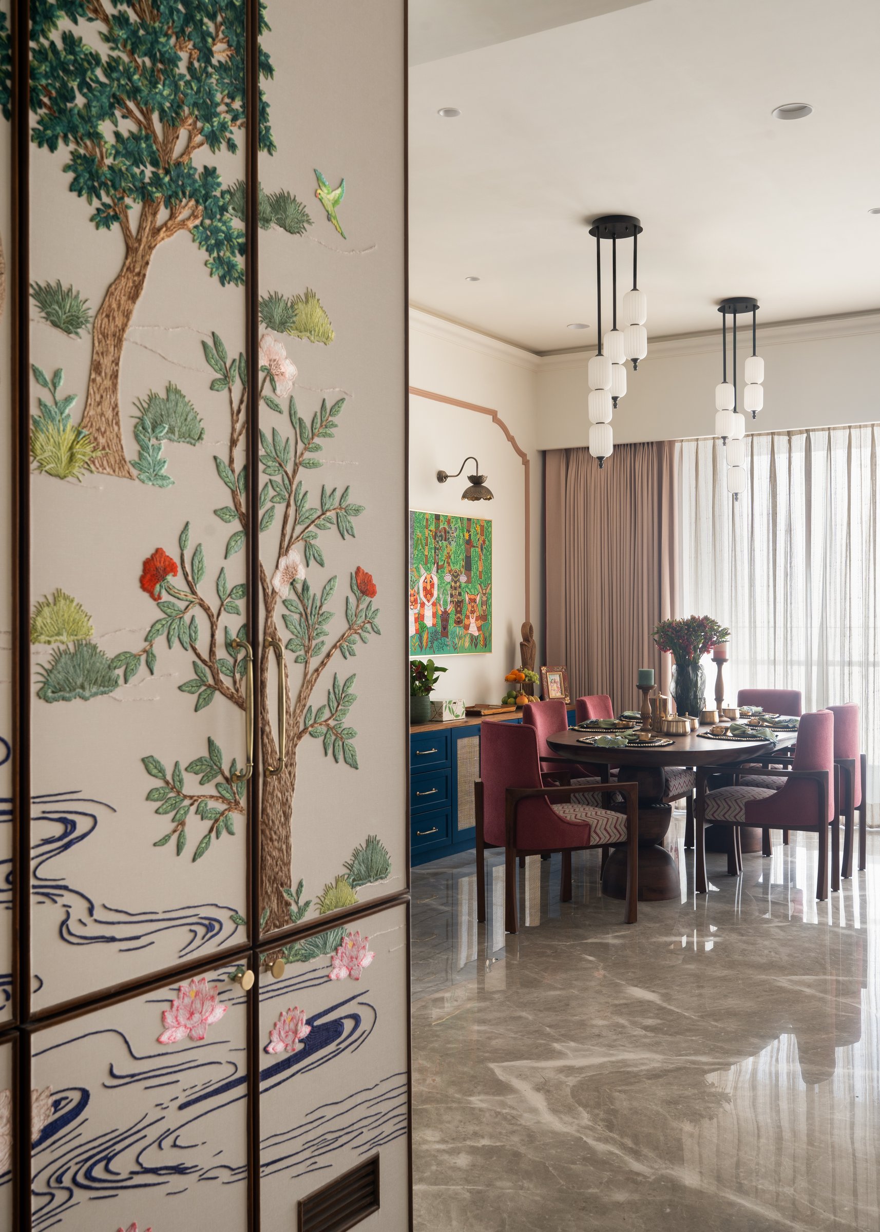 From foyer to dining: the embroidered cabinetry gives way to red chairs and a deep blue sideboard beyond