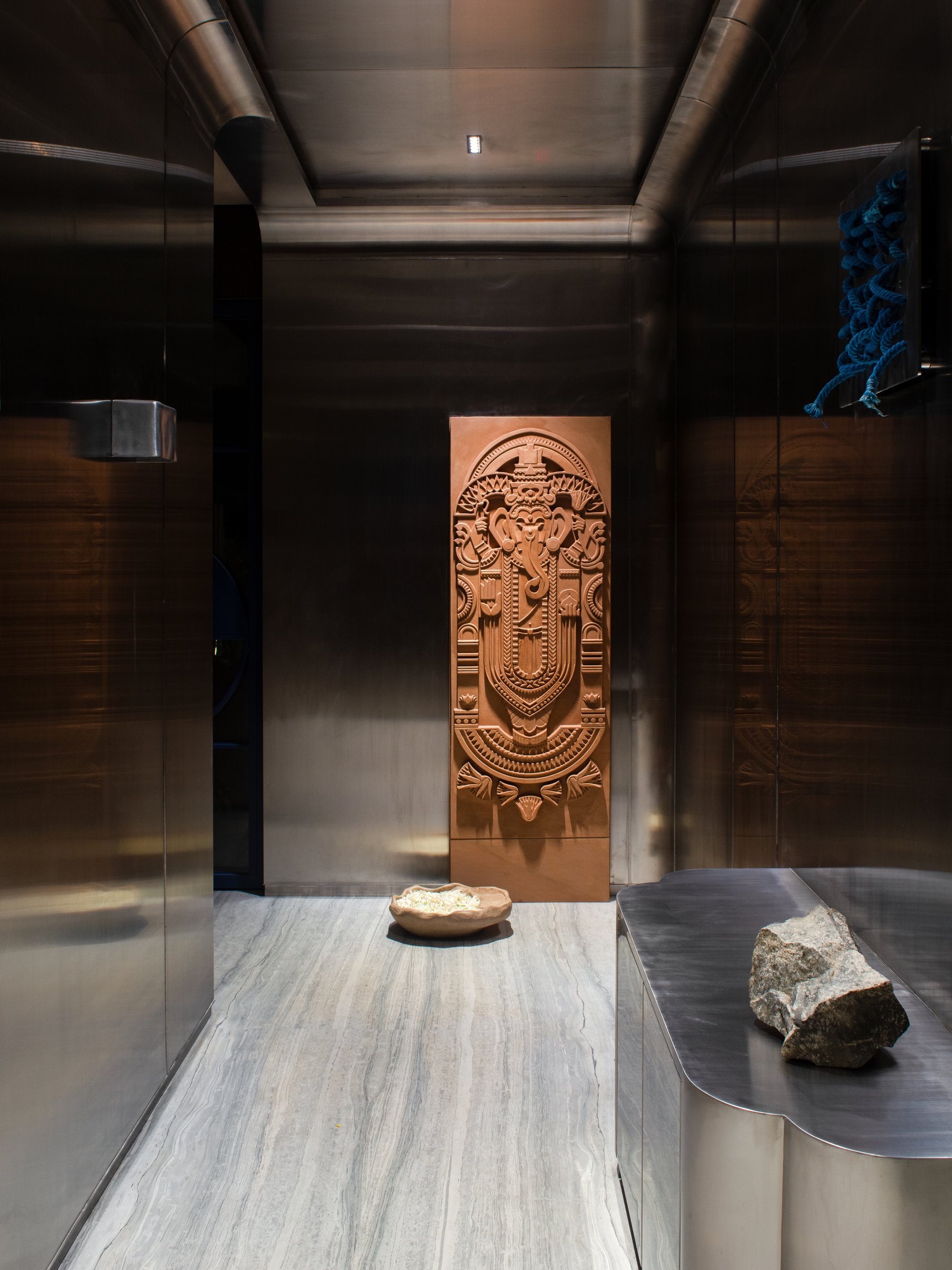 The entry foyer, where bronzed metallic walls frame a carved copper-toned deity panel and a sculpted stone bowl