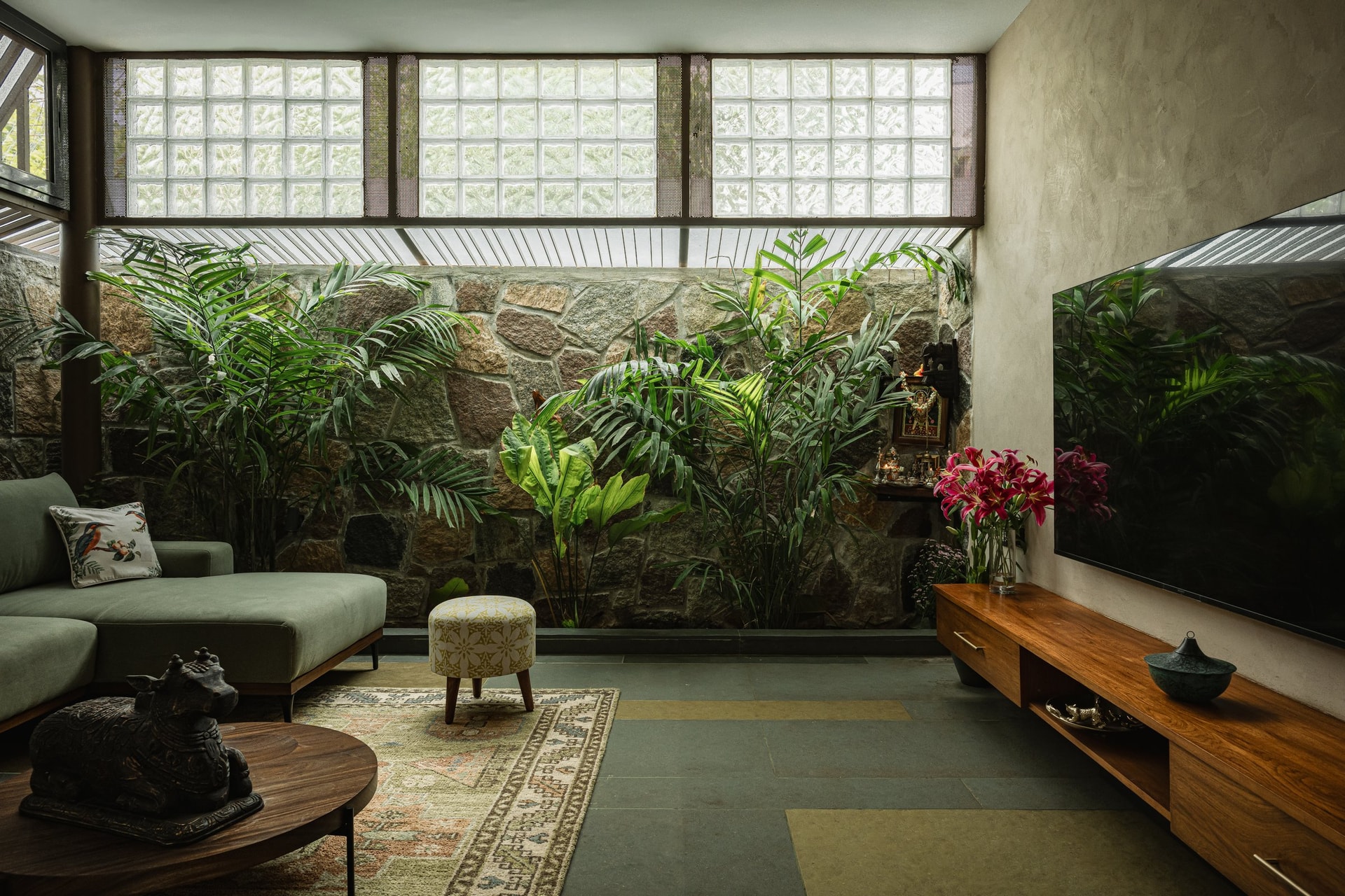 The living room turns toward an internal stone wall and planted pocket, lit by a clerestory of glass blocks