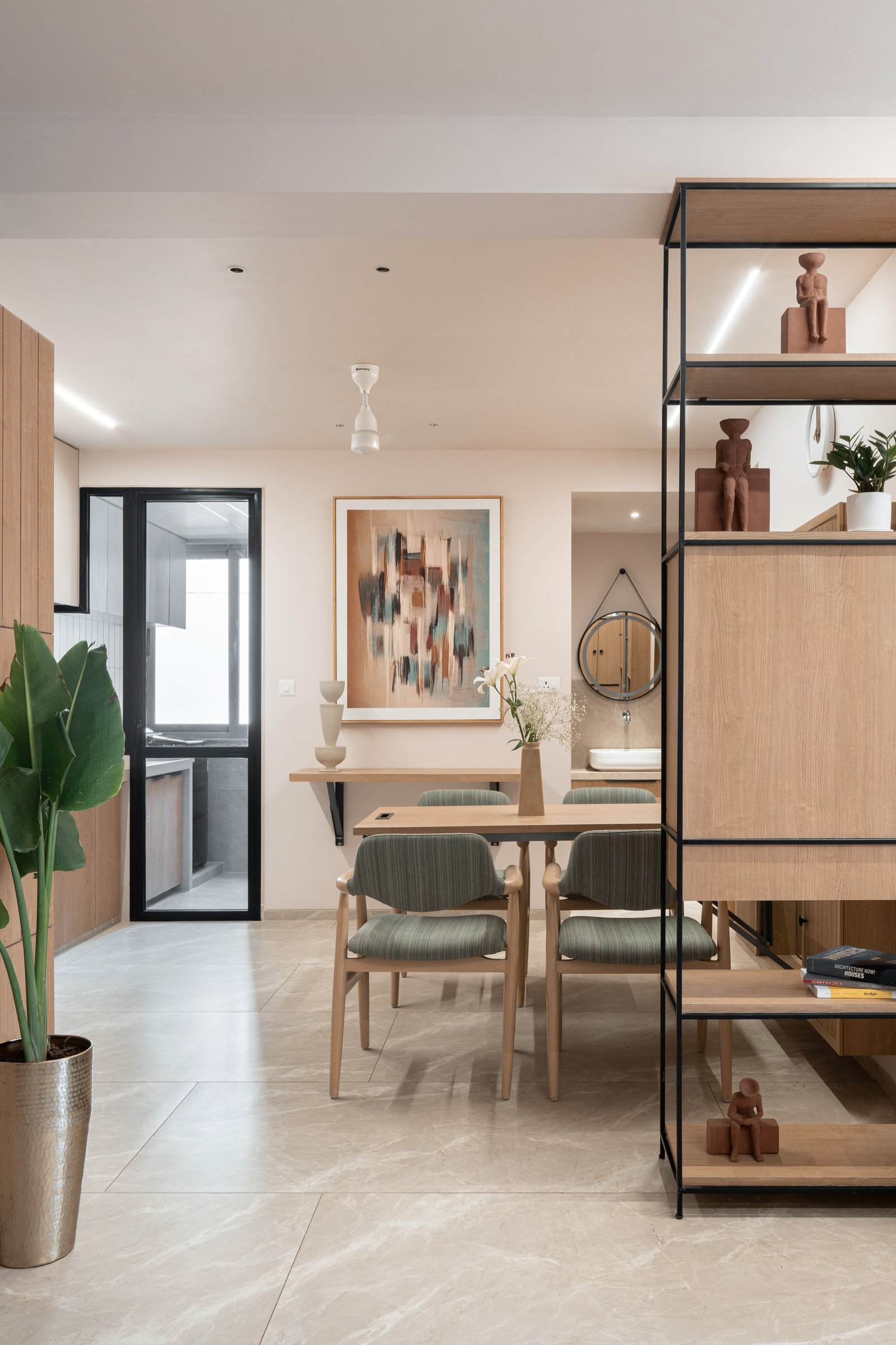 The dining area, anchored by an oak table and a metal-and-wood shelving unit holding terracotta figures and design books