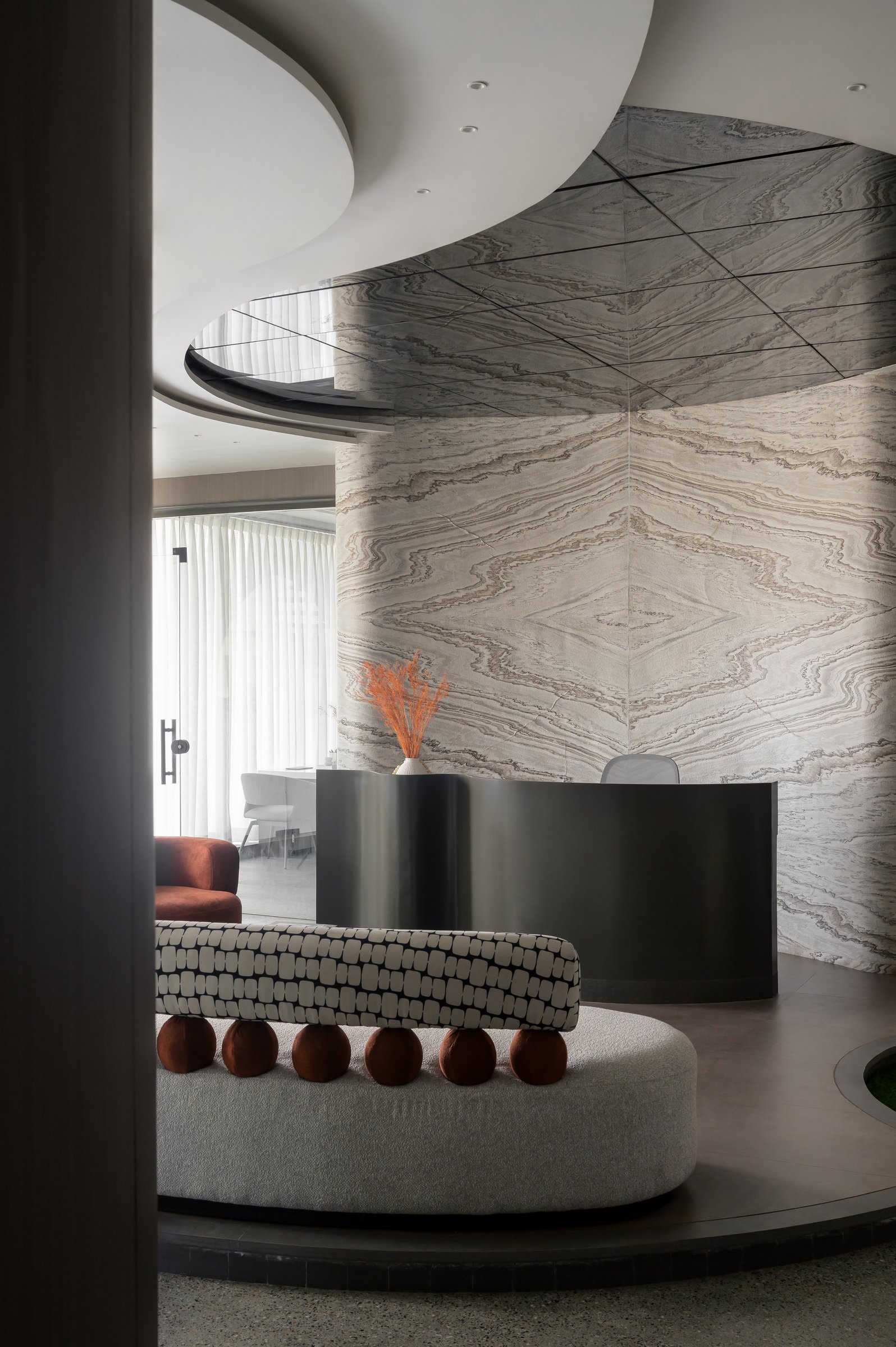 The curved metallic reception desk, set against book-matched stone that does the quiet work of artwork