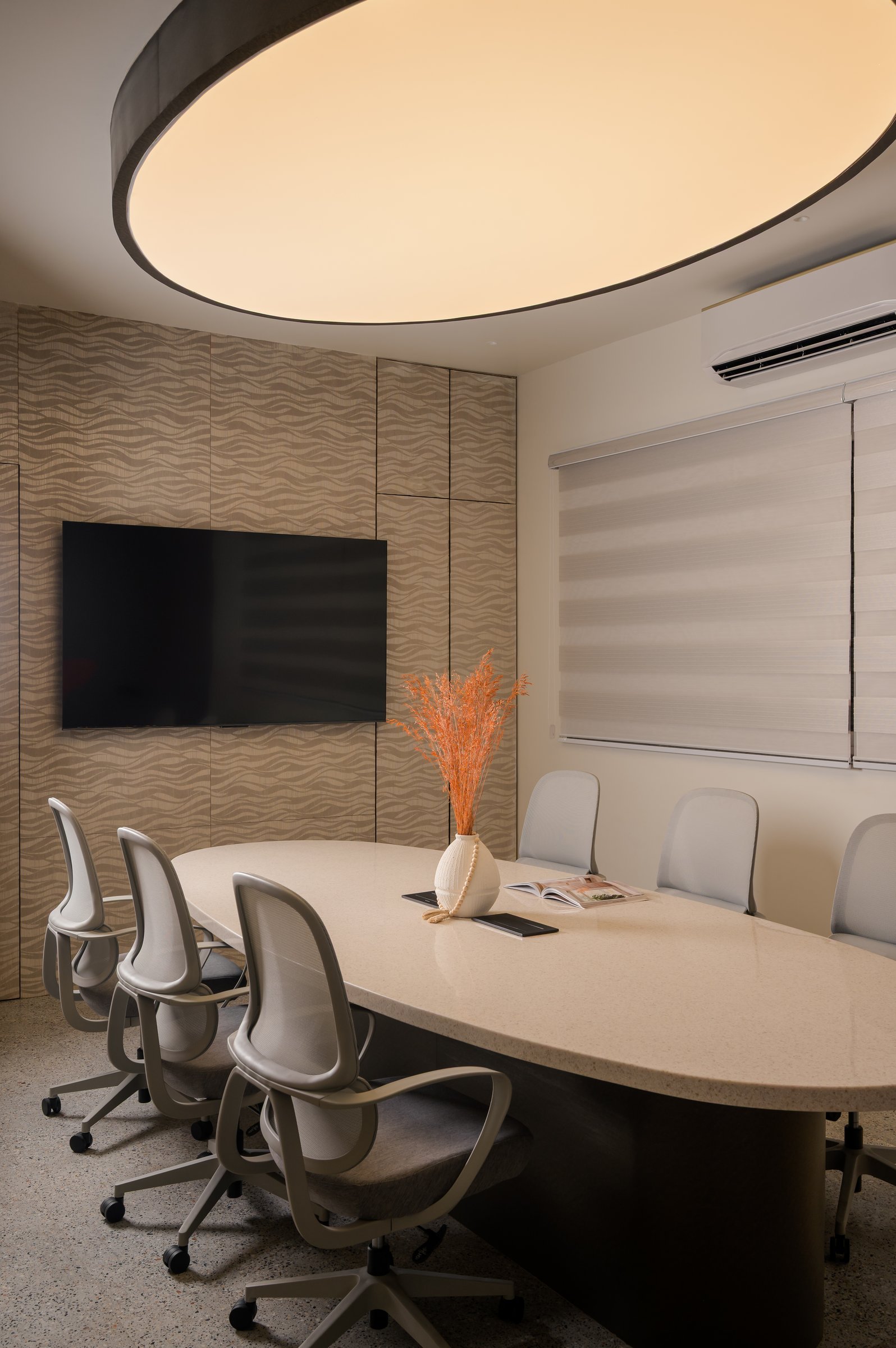 The conference room, where an oval table beneath a softly glowing oval light registers a quieter, more focused tone