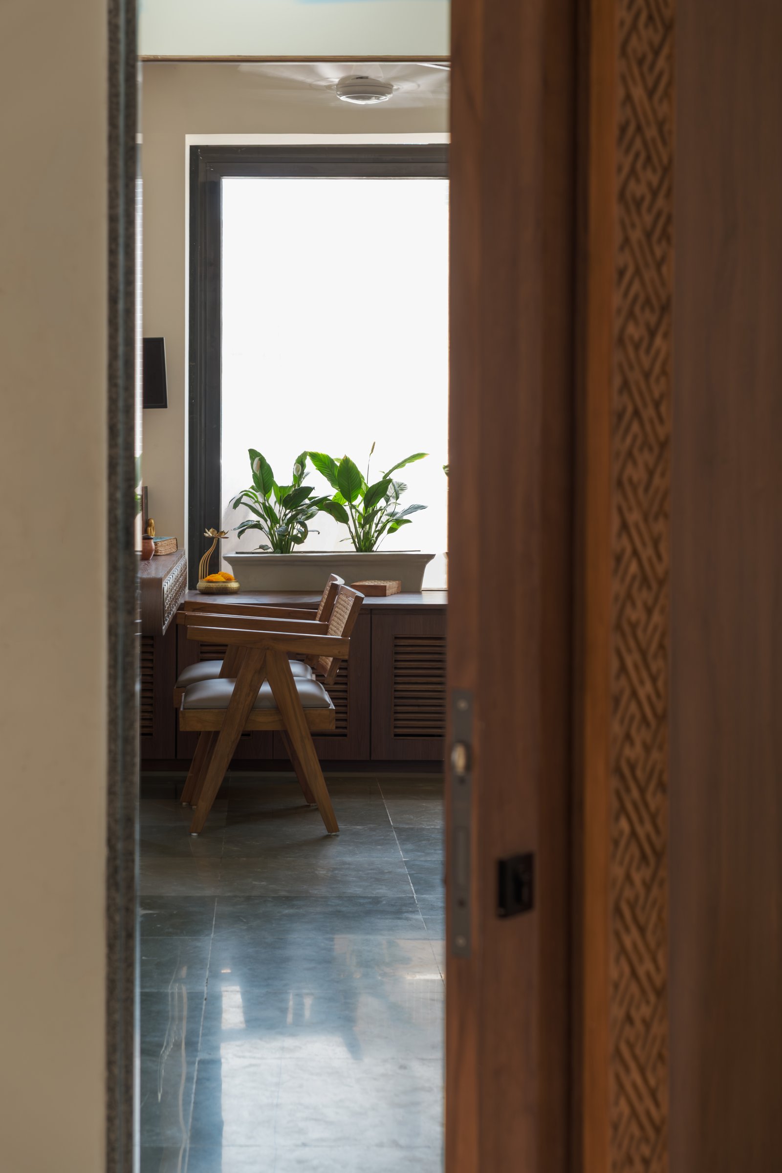The clinic glimpsed through a carved teak door, where Kota stone, dark teakwood louvres, and a planter of broad-leafed greens establish the material register
