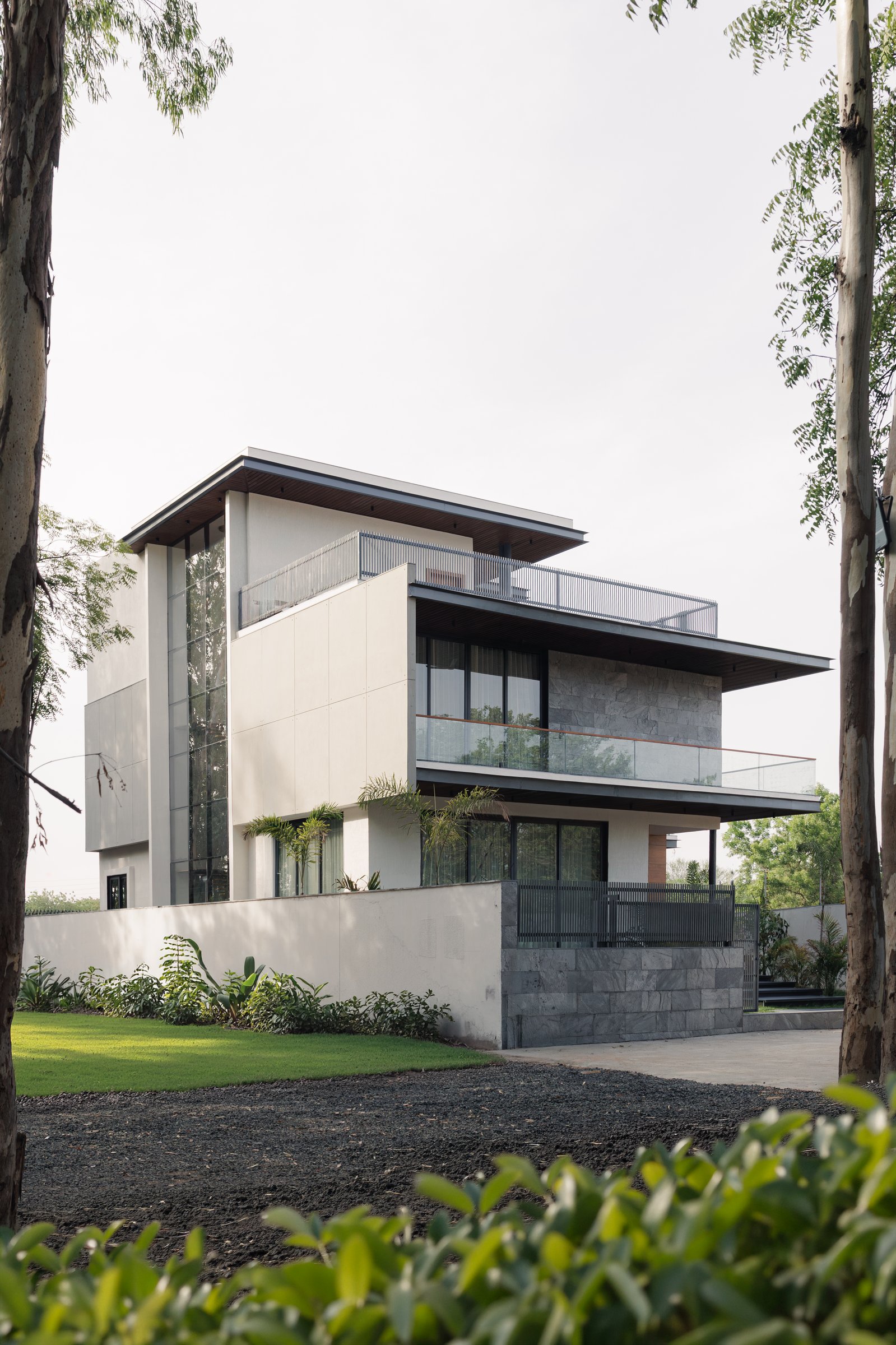 The garden elevation, cantilevered roof planes floating over a stone-clad plinth and a tall glazed corner volume