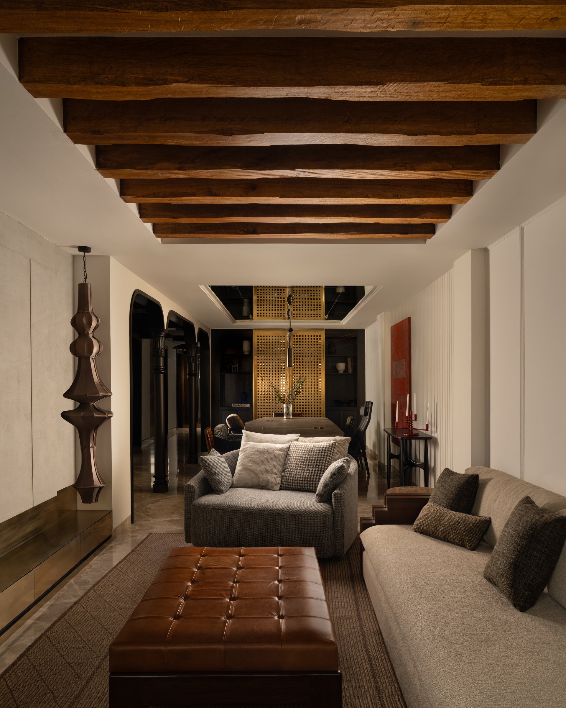 The living room, where hand-hewn wooden rafters and a sculptural metallic pendant set the tone for the home's reliance on singular, oversized gestures