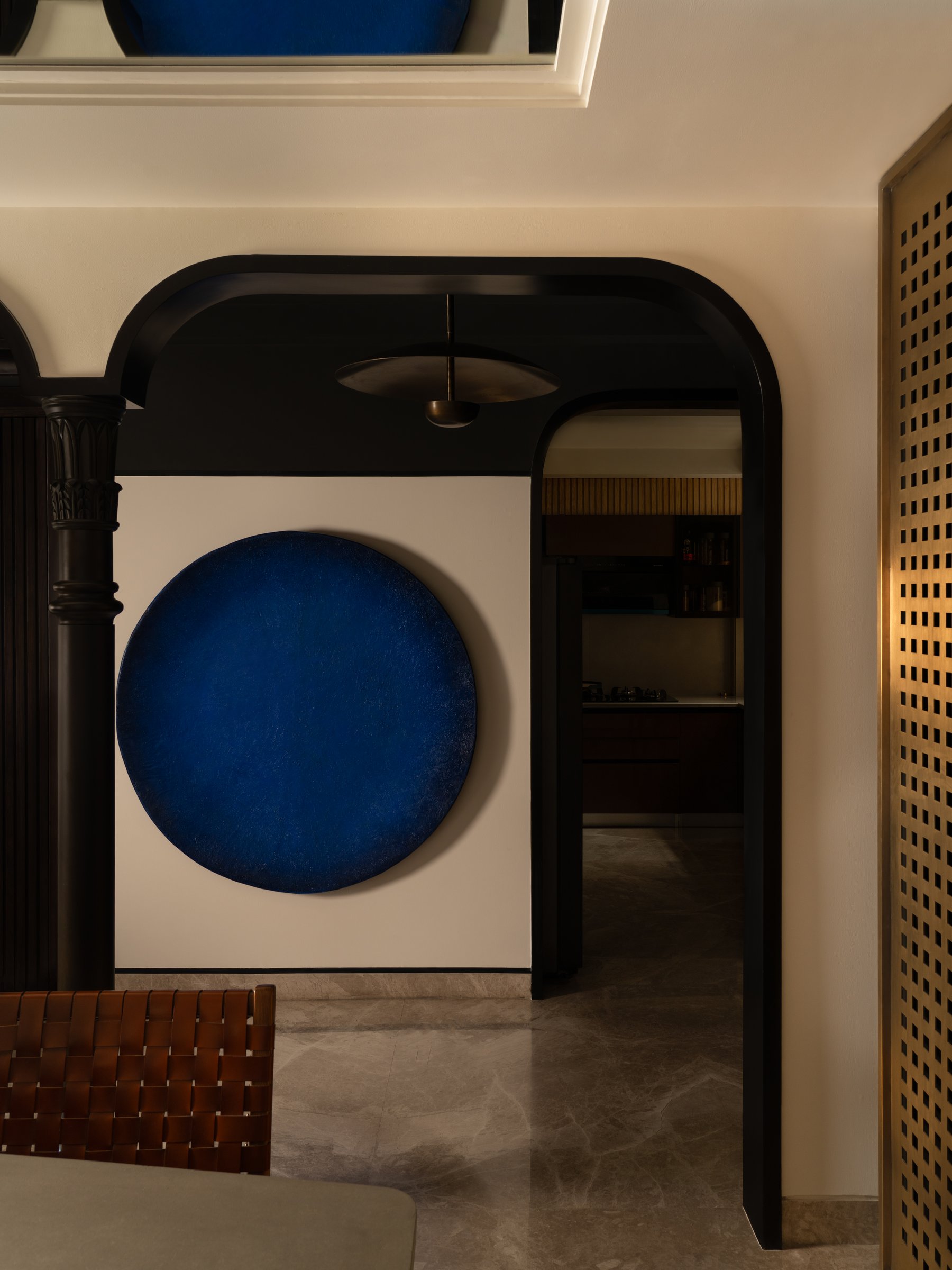 A blackened archway frames a circular blue artwork by Mayank Goyal, with a brass perforated screen filtering light into the dining beyond