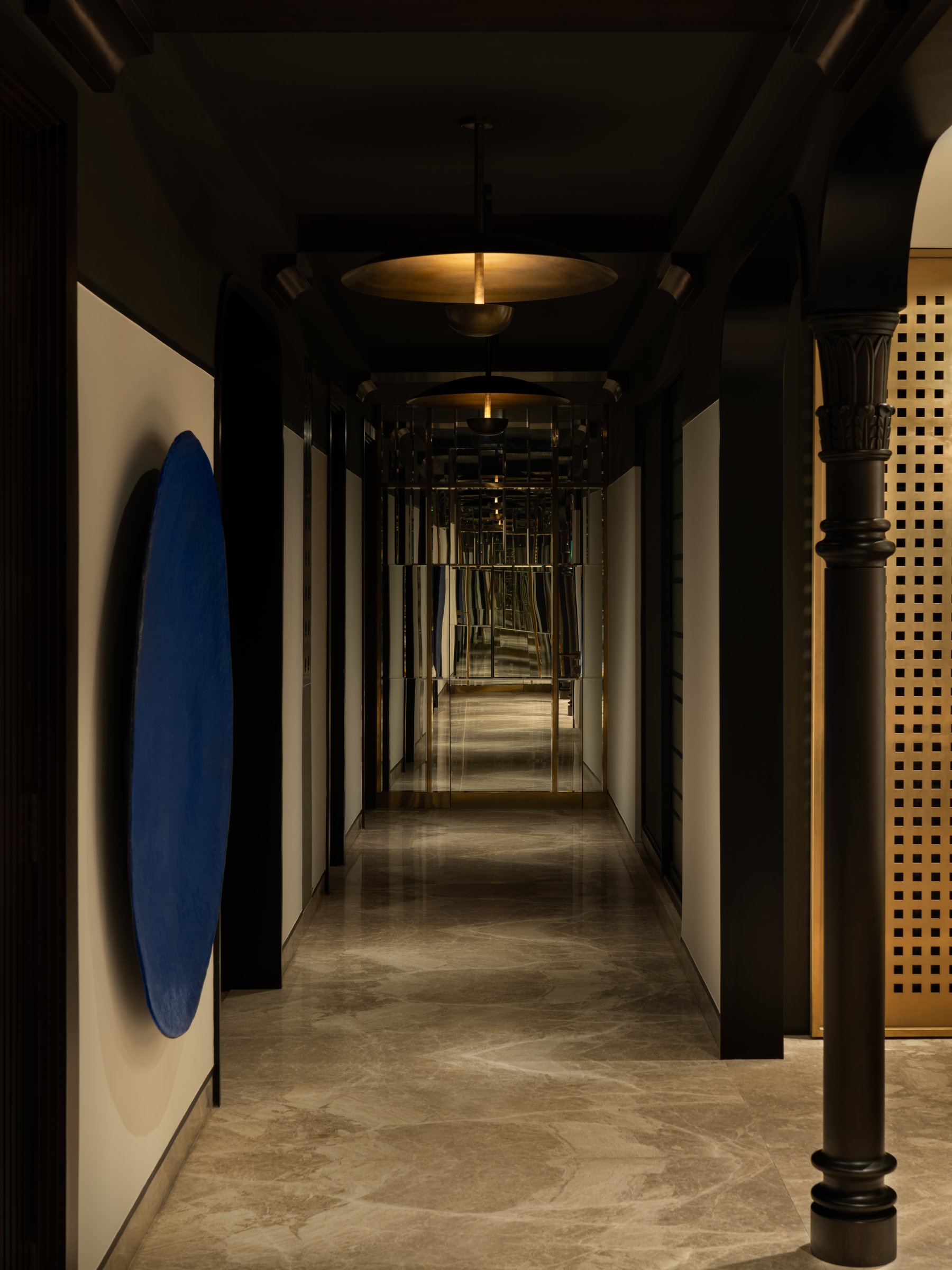 The corridor as spine, its charcoal ceiling and brass pendants drawing the eye toward mirror-mosaic bedroom doors