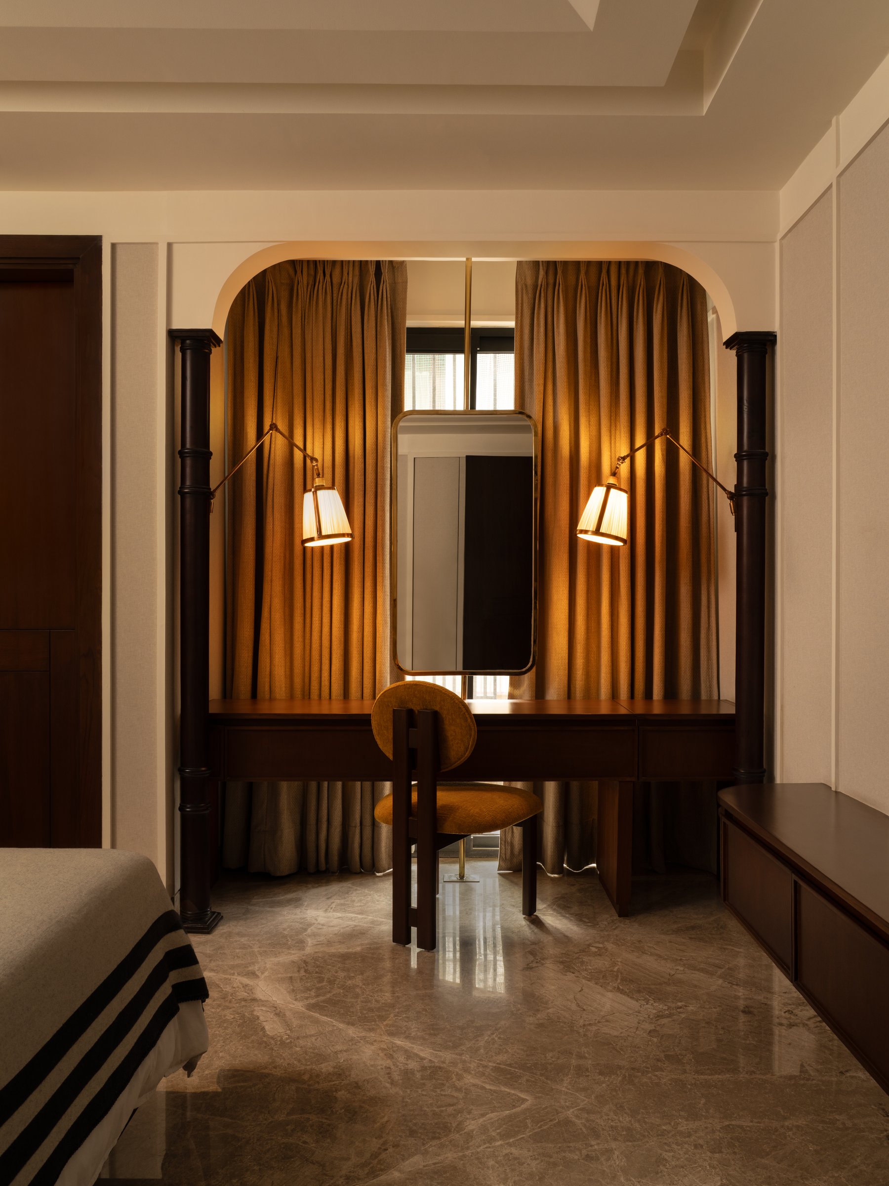 A dressing nook set into an arched recess, framed by slim dark columns and pleated curtains, treats a functional vanity as architectural event