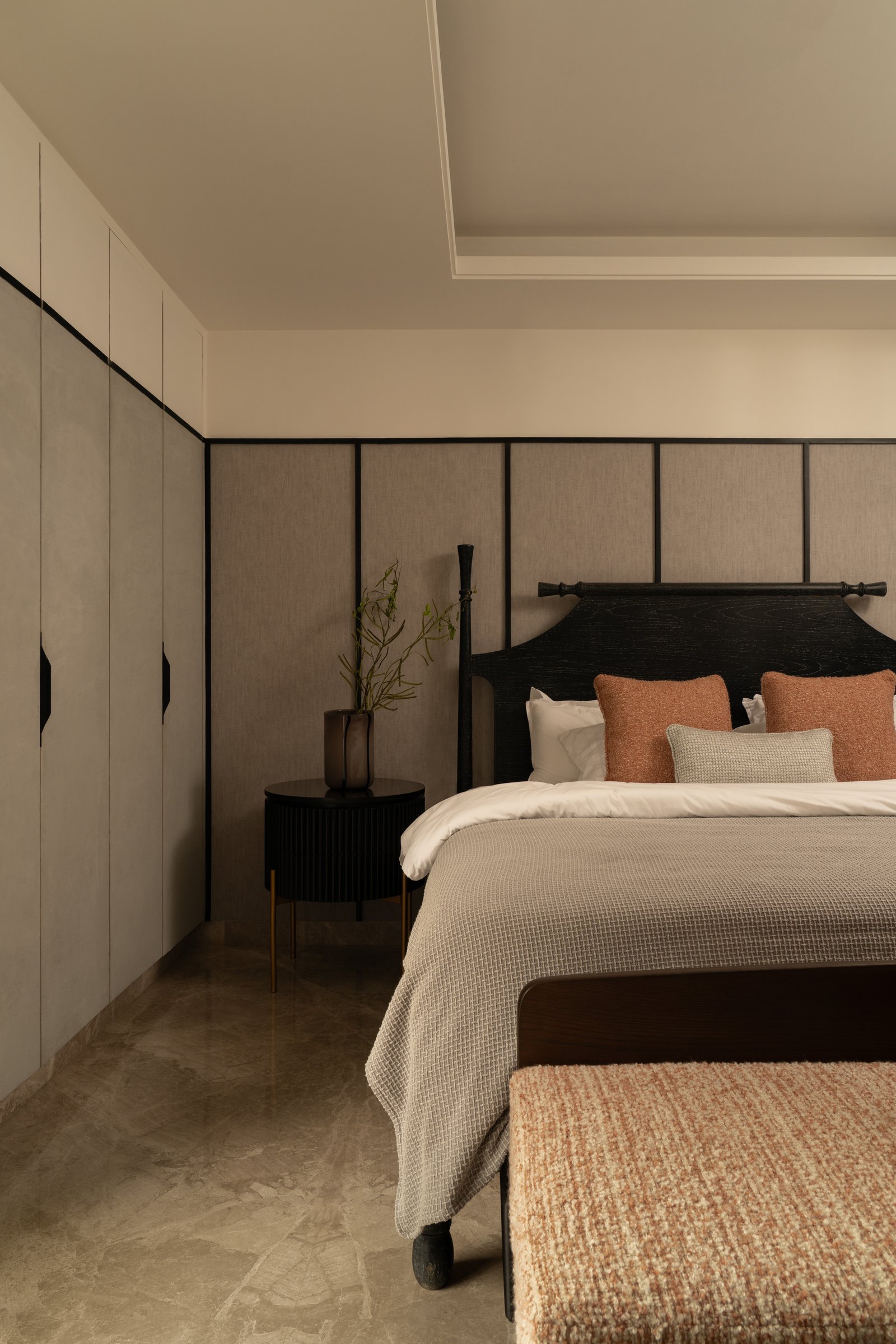 The master bedroom, where an upholstered headboard wall and a dark fluted bedside cabinet introduce a warmer, more tactile register