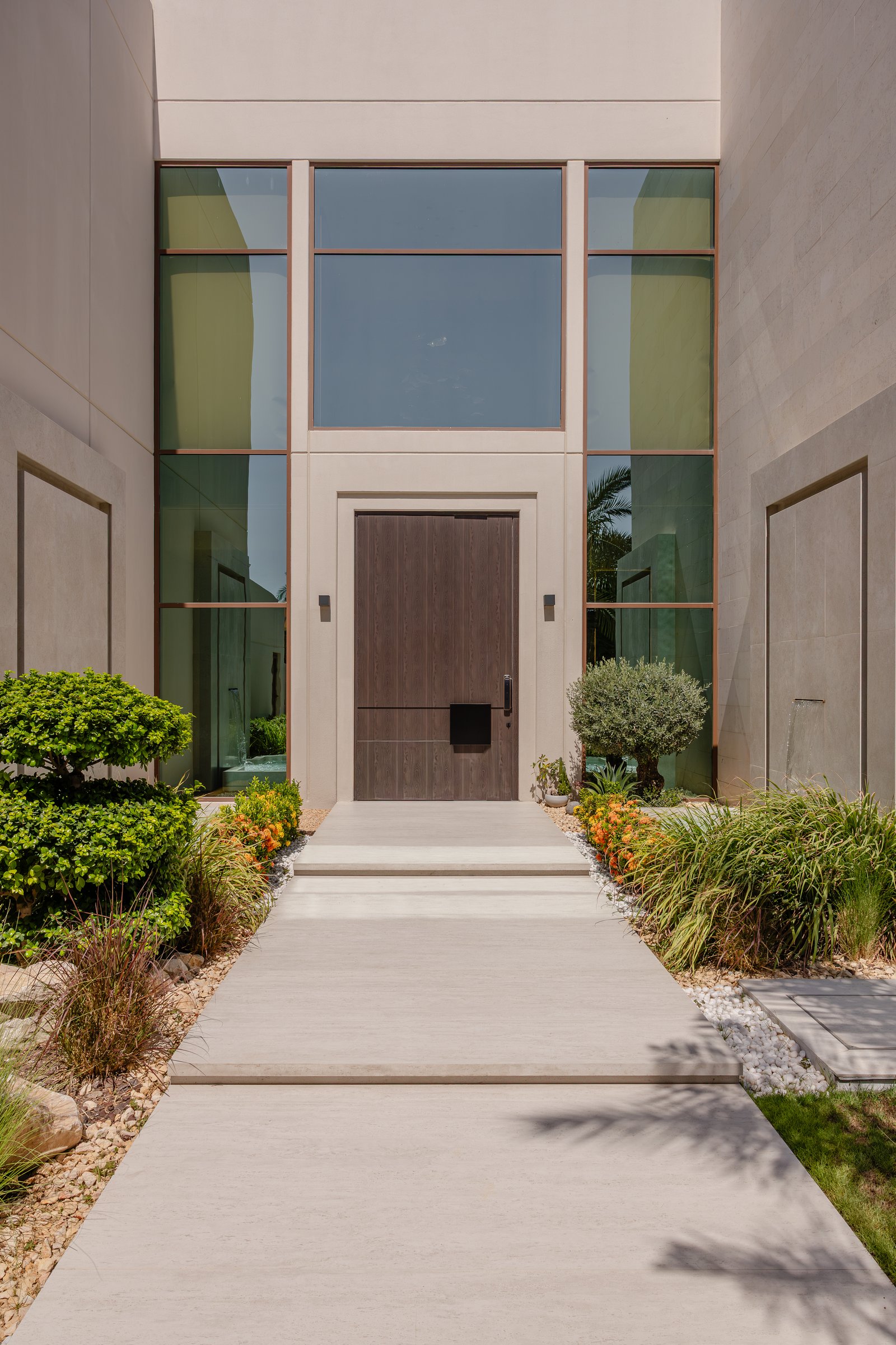 The entry approach, where a dark wood pivot door and tall glazed screen establish the home's restrained architectural language