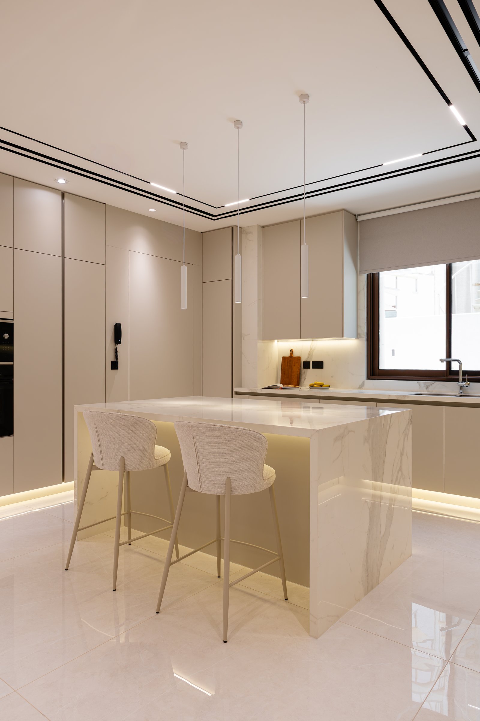 The kitchen, where a veined stone island and integrated cove lighting anchor a quiet palette of neutral cabinetry