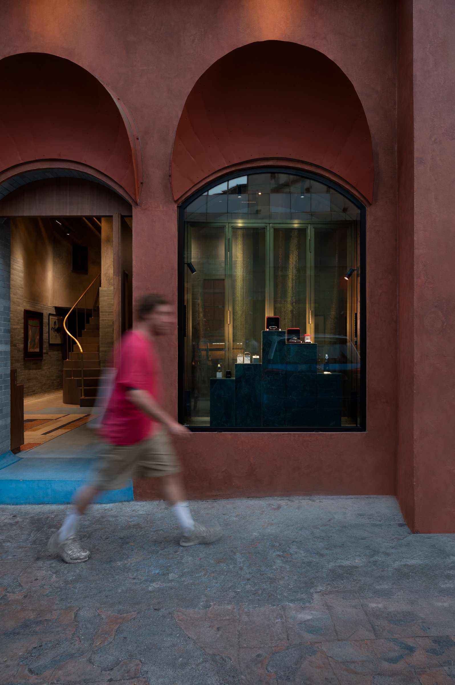 The arched shopfront window, framing dark green display plinths and softly lit vitrines behind arched glass