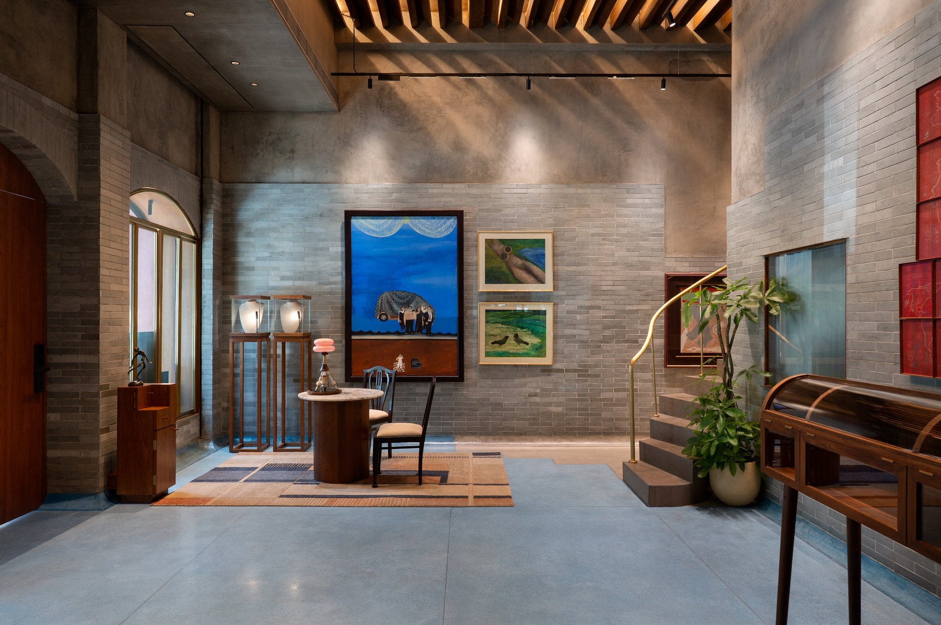 The double-height retail floor beneath the reclaimed teak girder ceiling, anchored by a patchwork rug and a large blue painting