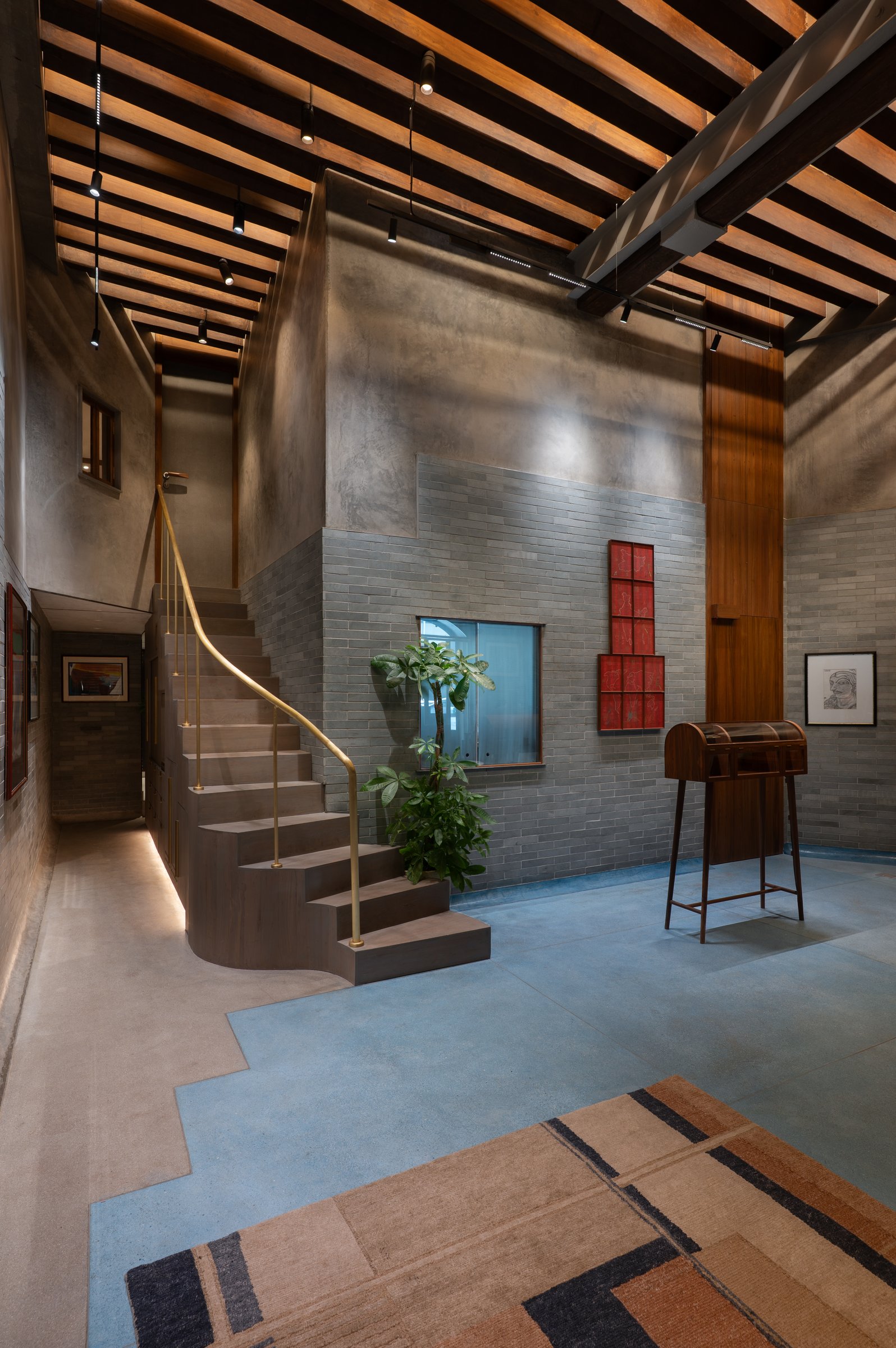 The sculptural mezzanine stair, a dark stained flight drawn upward by a single continuous brass balustrade