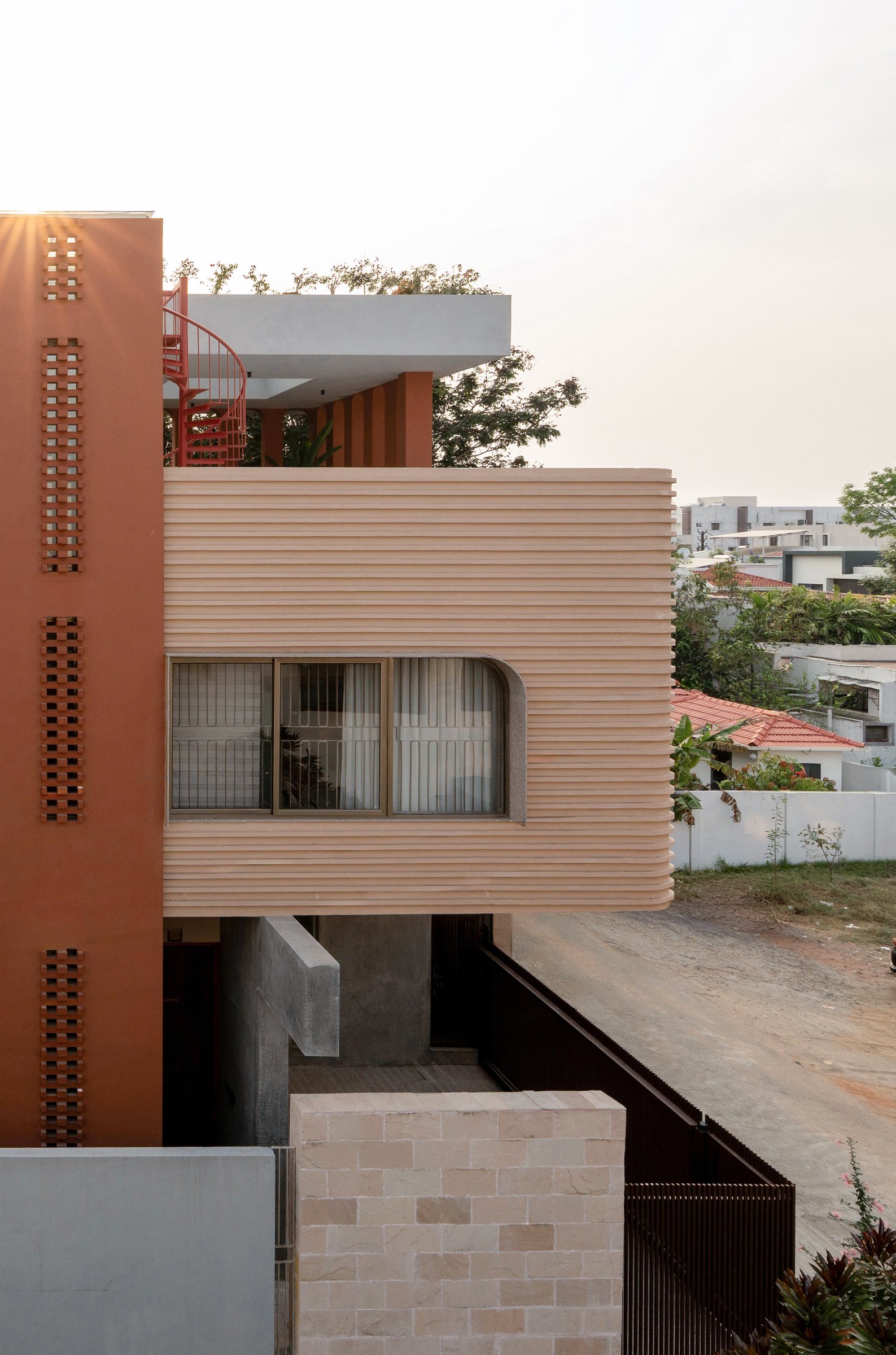 A raised view of the upper volumes, revealing the ribbed cantilever, terracotta fins, and the coral spiral stair on the terrace