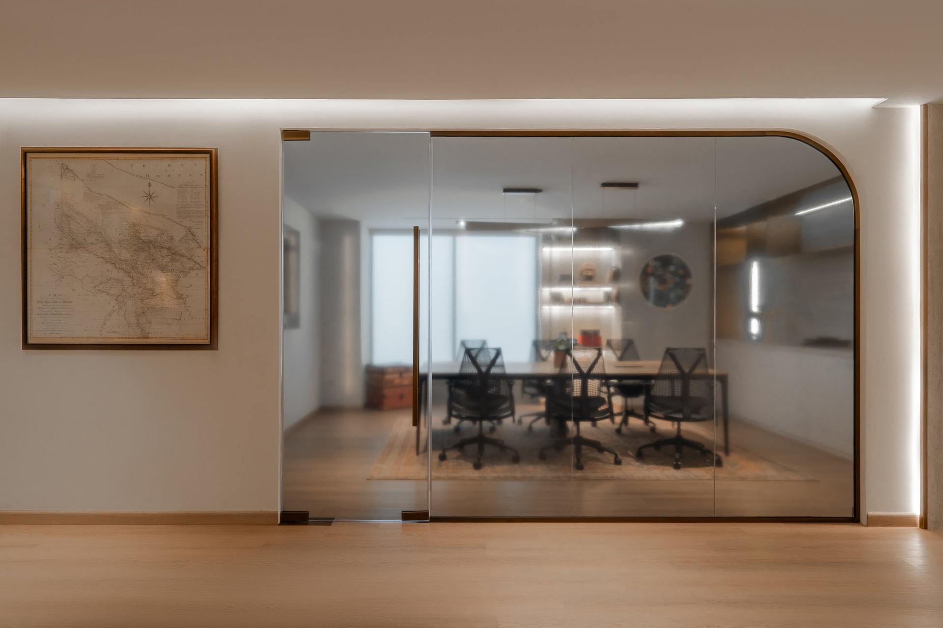 The threshold to the primary meeting room, where a framed antique map and a warm-metal arched glass partition set the interior's opening tone
