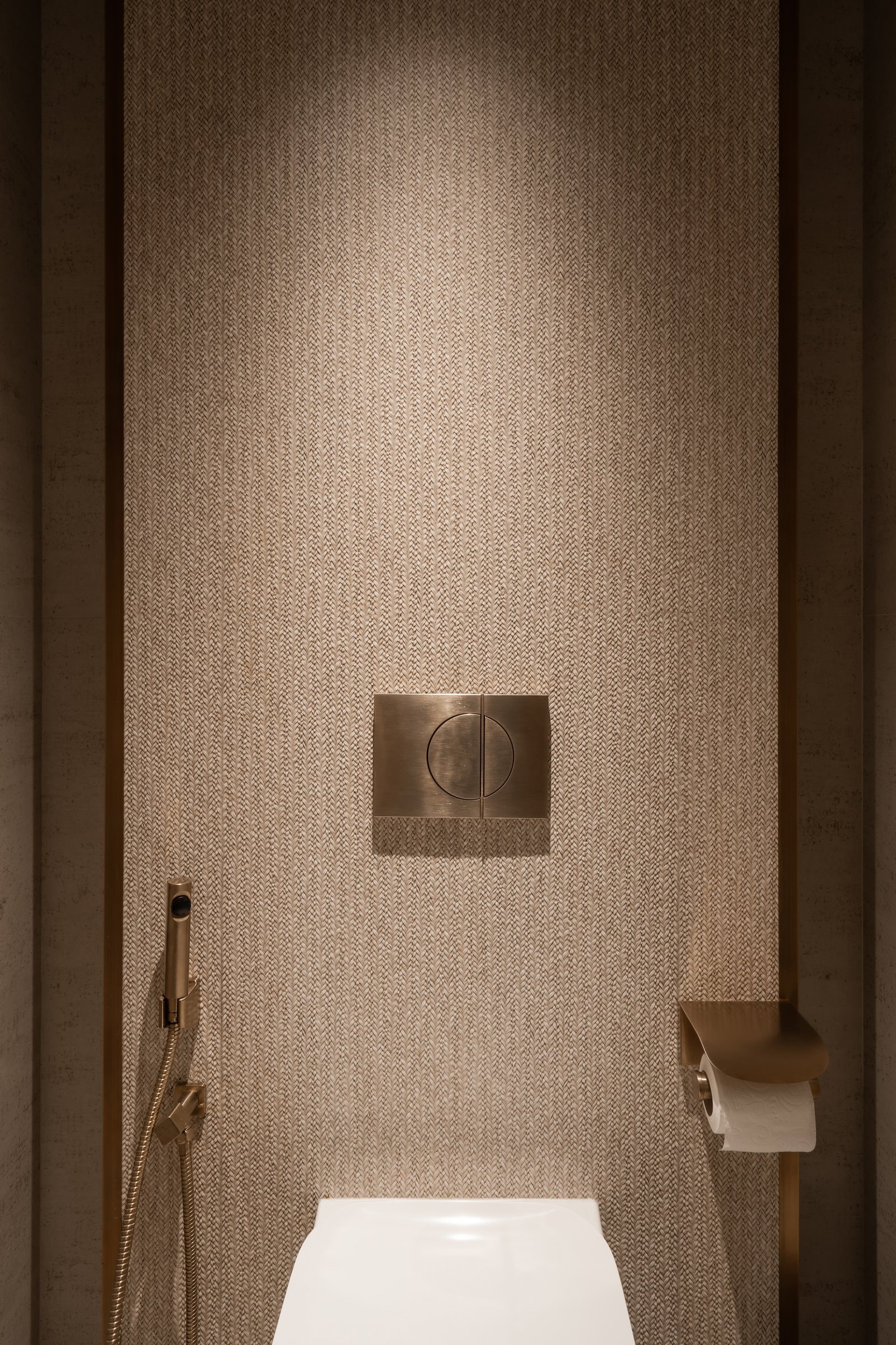 A herringbone-weave wall covering meets a brushed metal flush plate in the powder room's most private corner