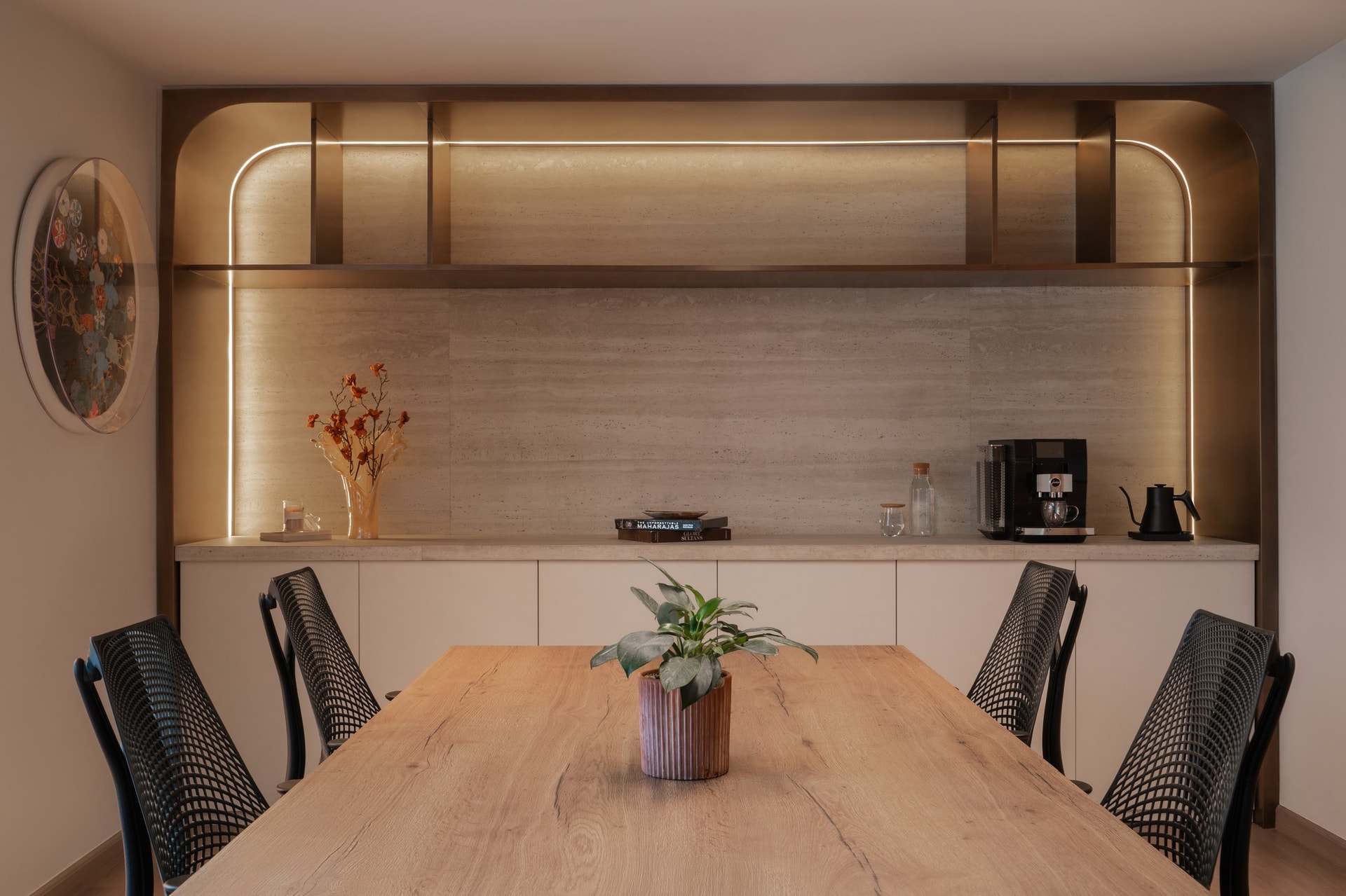 The coffee counter, set within a warm-metal arch, translates a residential sideboard into workplace vocabulary