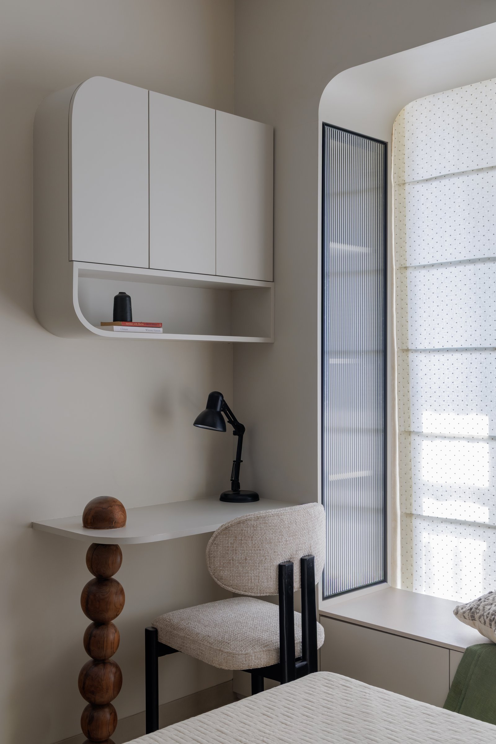 The study nook within the guest bedroom, its rounded storage unit and turned wooden pedestal echoing the dining table's silhouette