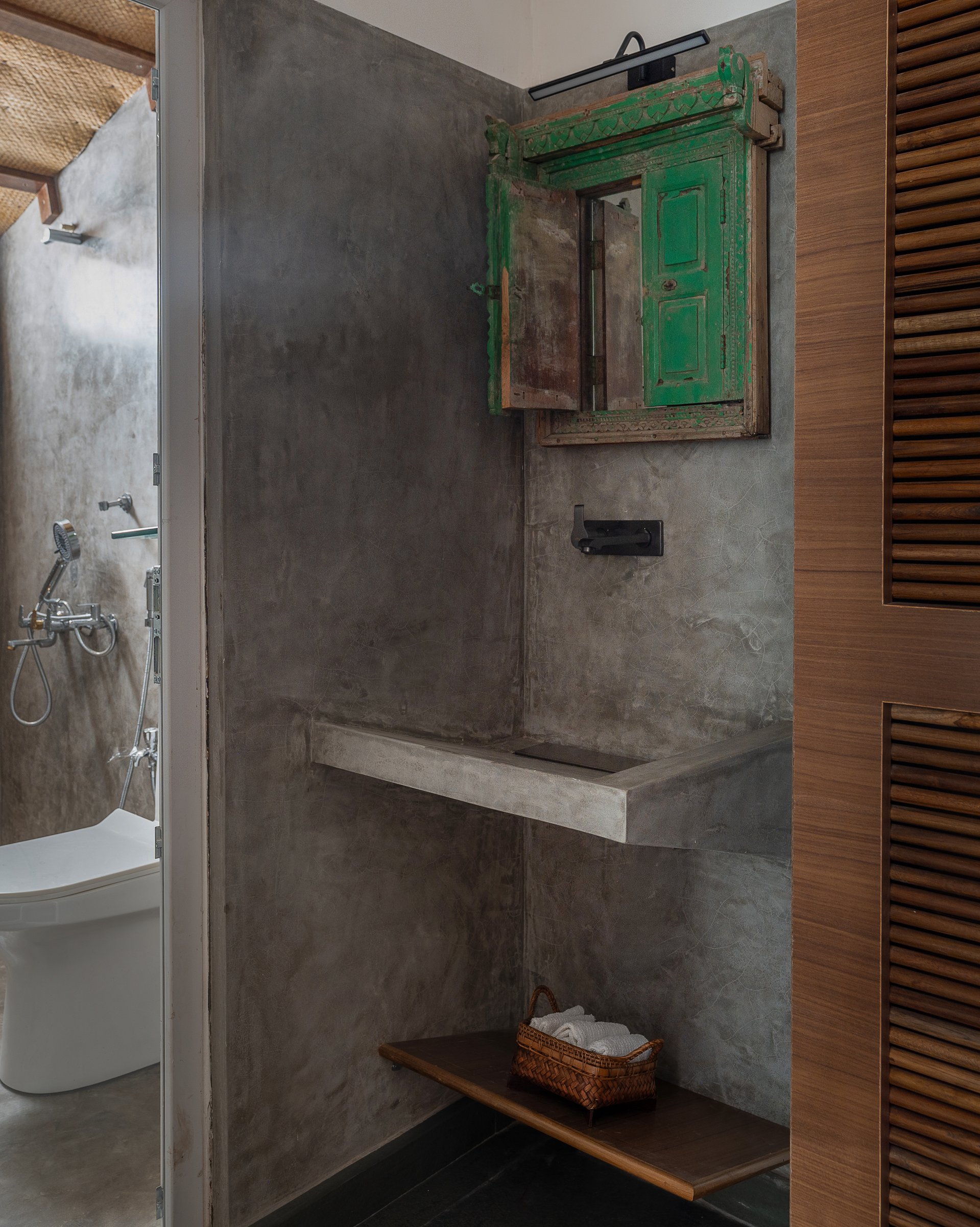 The bathroom, where a salvaged green timber window frame becomes the mirror surround above a cast oxide shelf