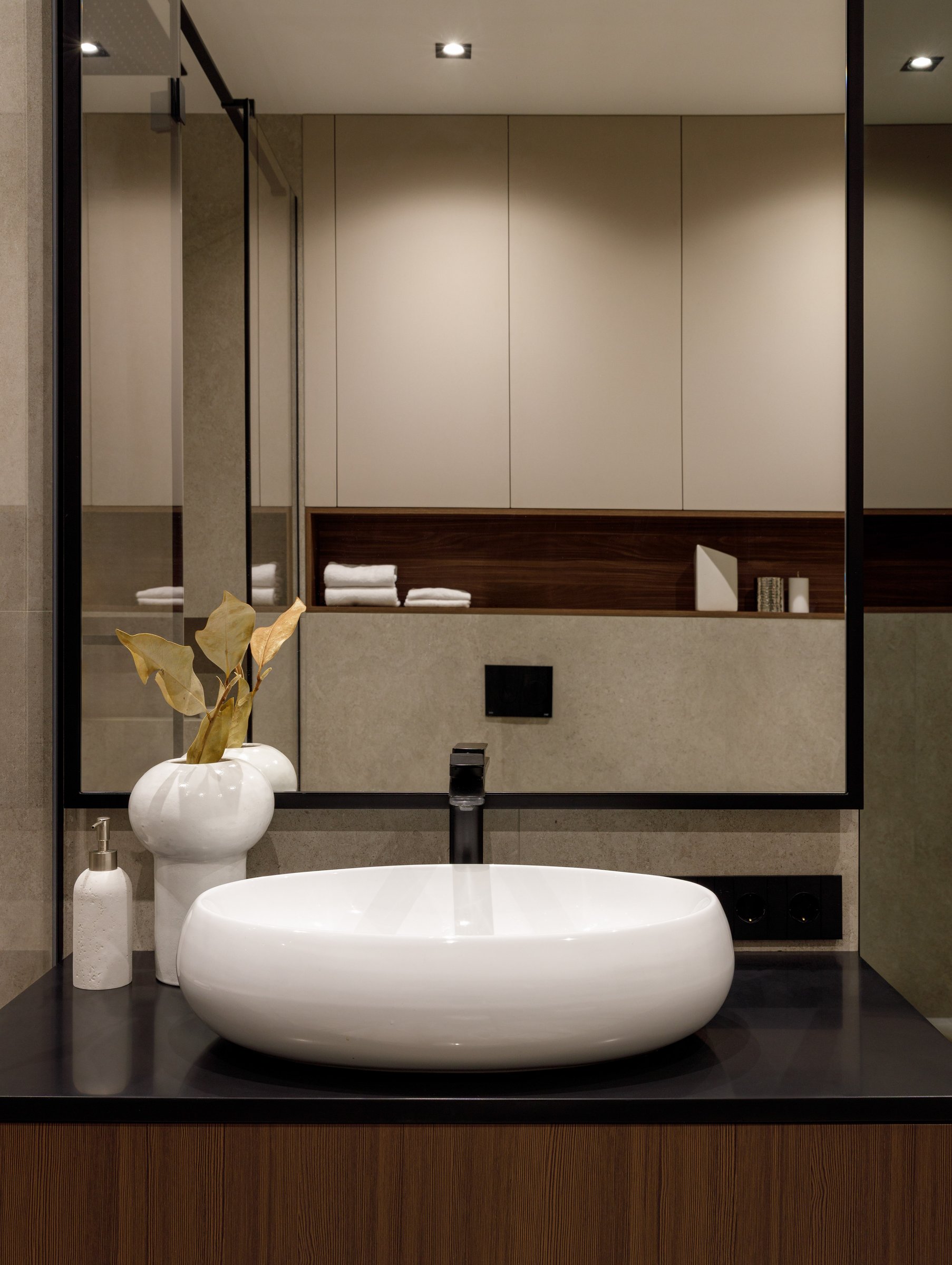 The powder room, where warm walnut and dark stone frame a rounded ceramic vessel