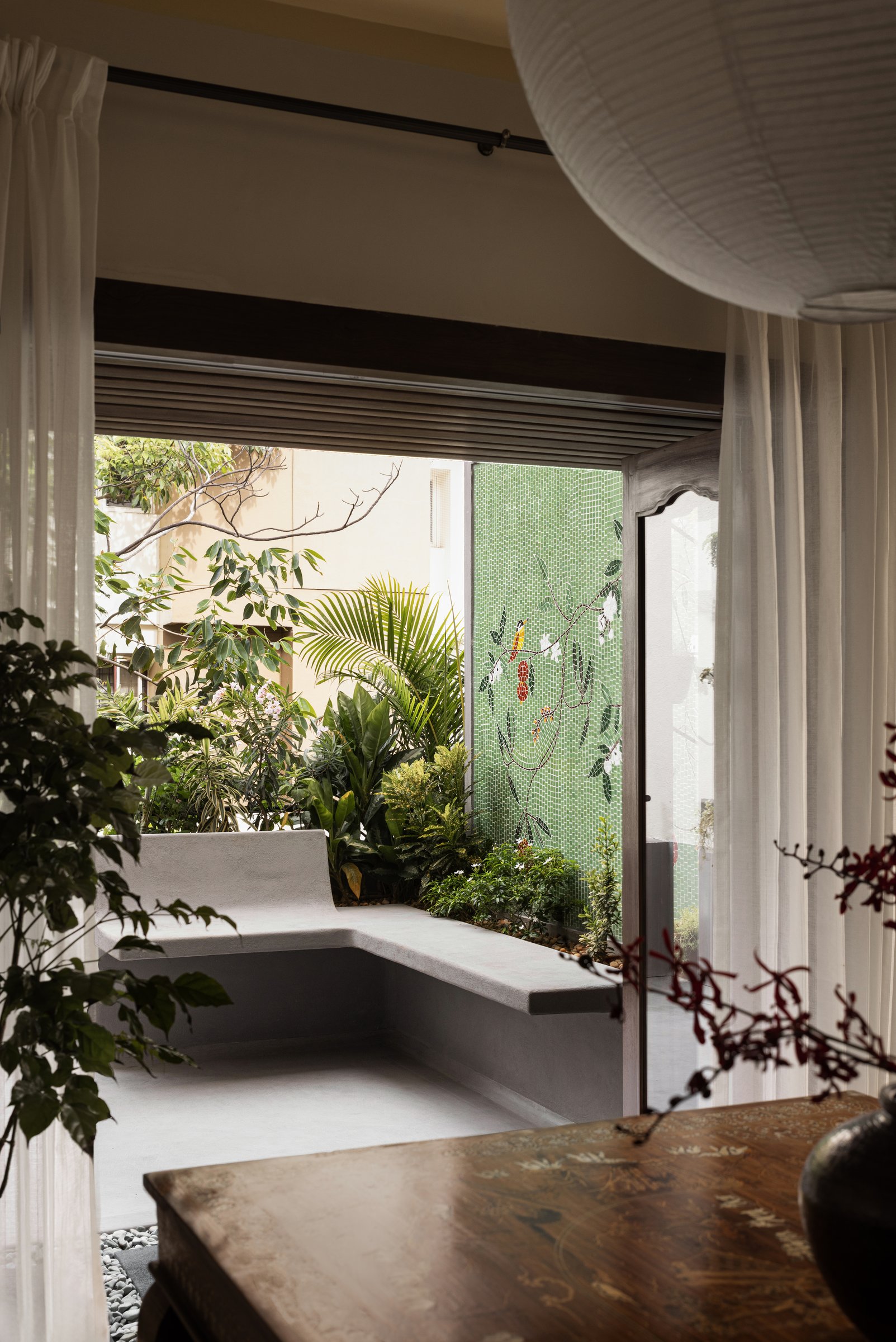 The threshold to a small planted courtyard, where a concrete bench turns against a green mosaic wall