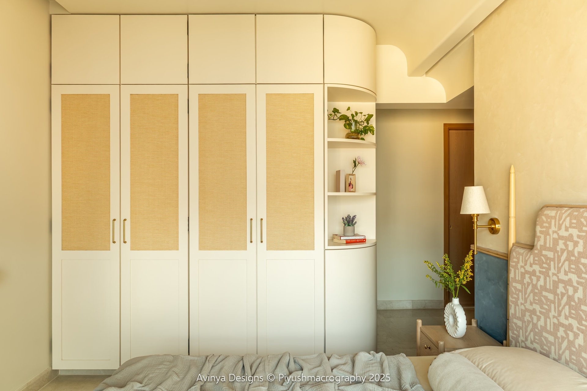 The master bedroom wardrobe wall, its cane-webbed cabinets meeting a rounded corner column of open shelves