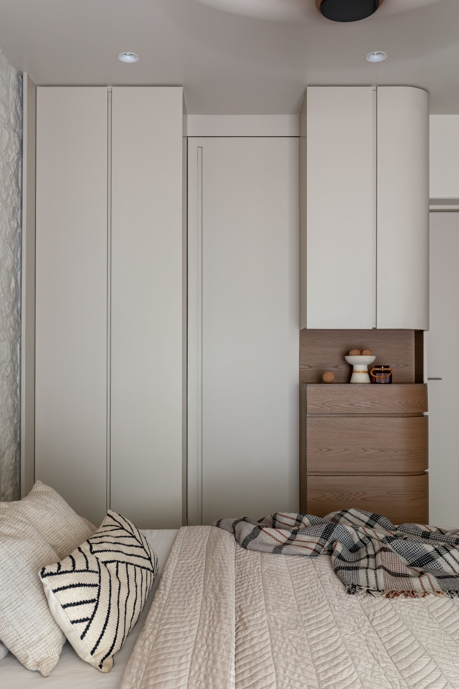 Full-height cabinetry meets a warm timber chest of drawers, the only expressed material break in an otherwise quiet room
