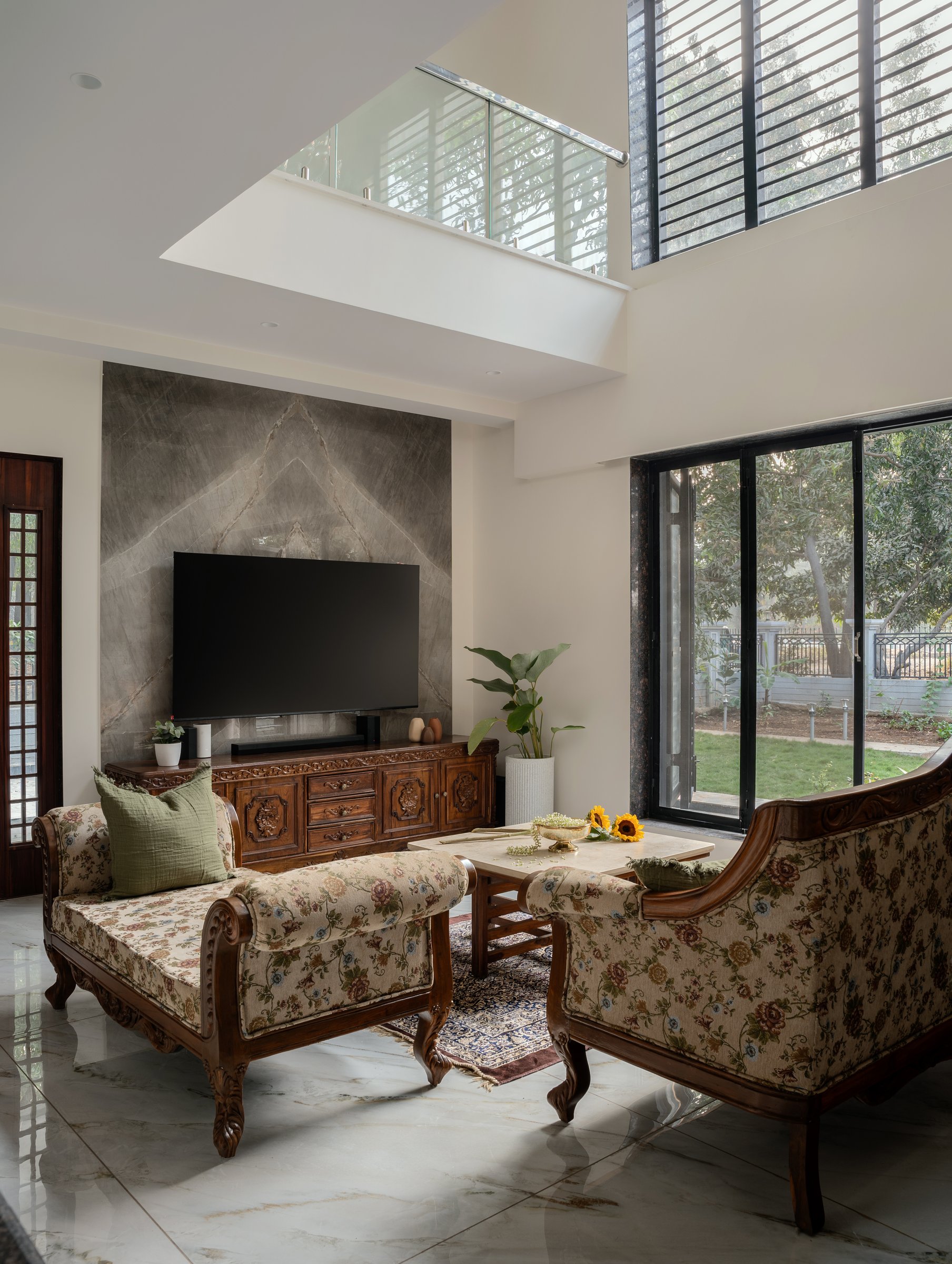 The double-height living room, where a bookmatched marble media wall meets carved Kerala-style seating