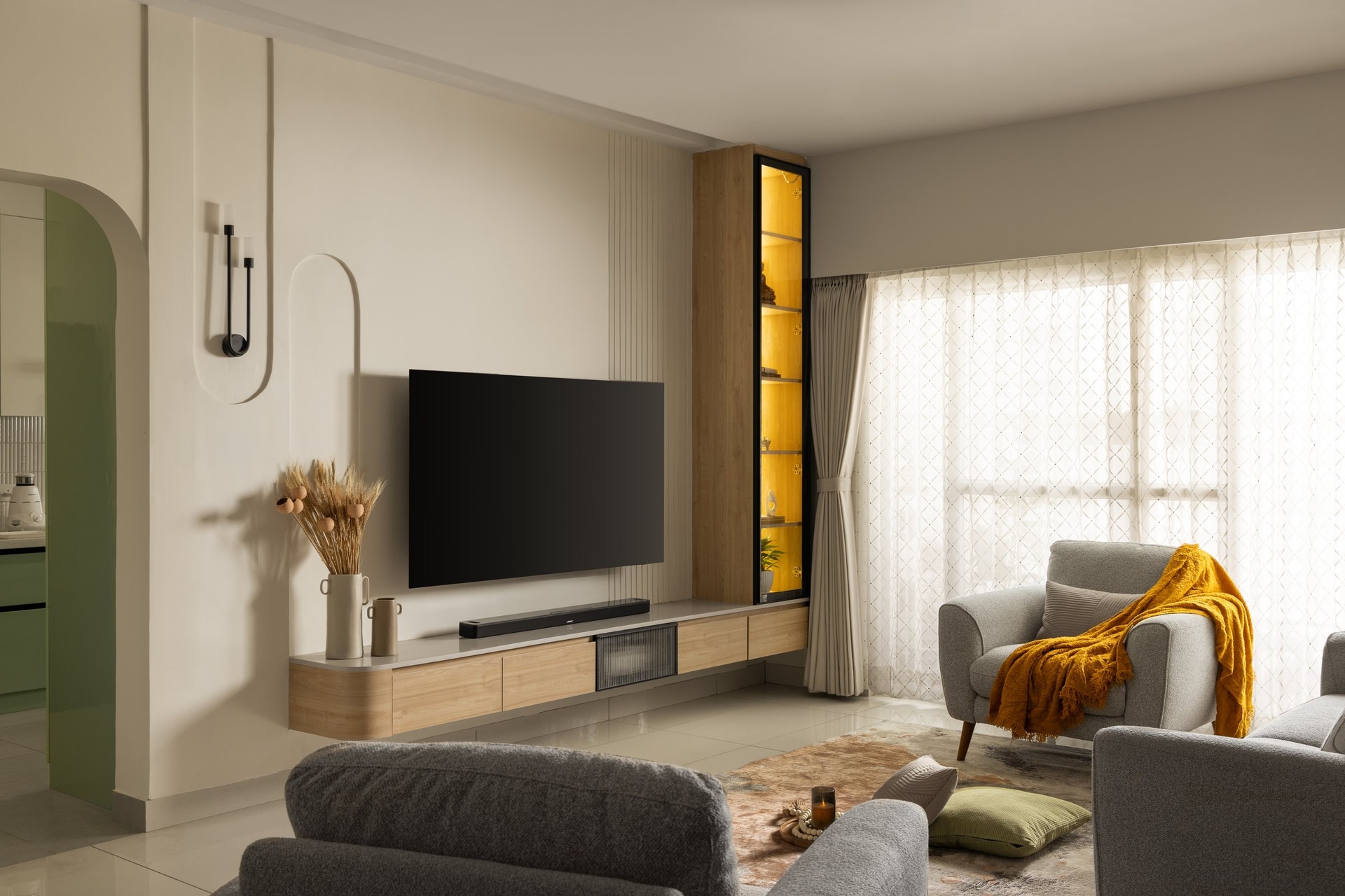 The living room's media wall, its plaster reveal and floating wood console setting the language of soft geometry, with a glimpse of the green-lacquered kitchen arch beyond