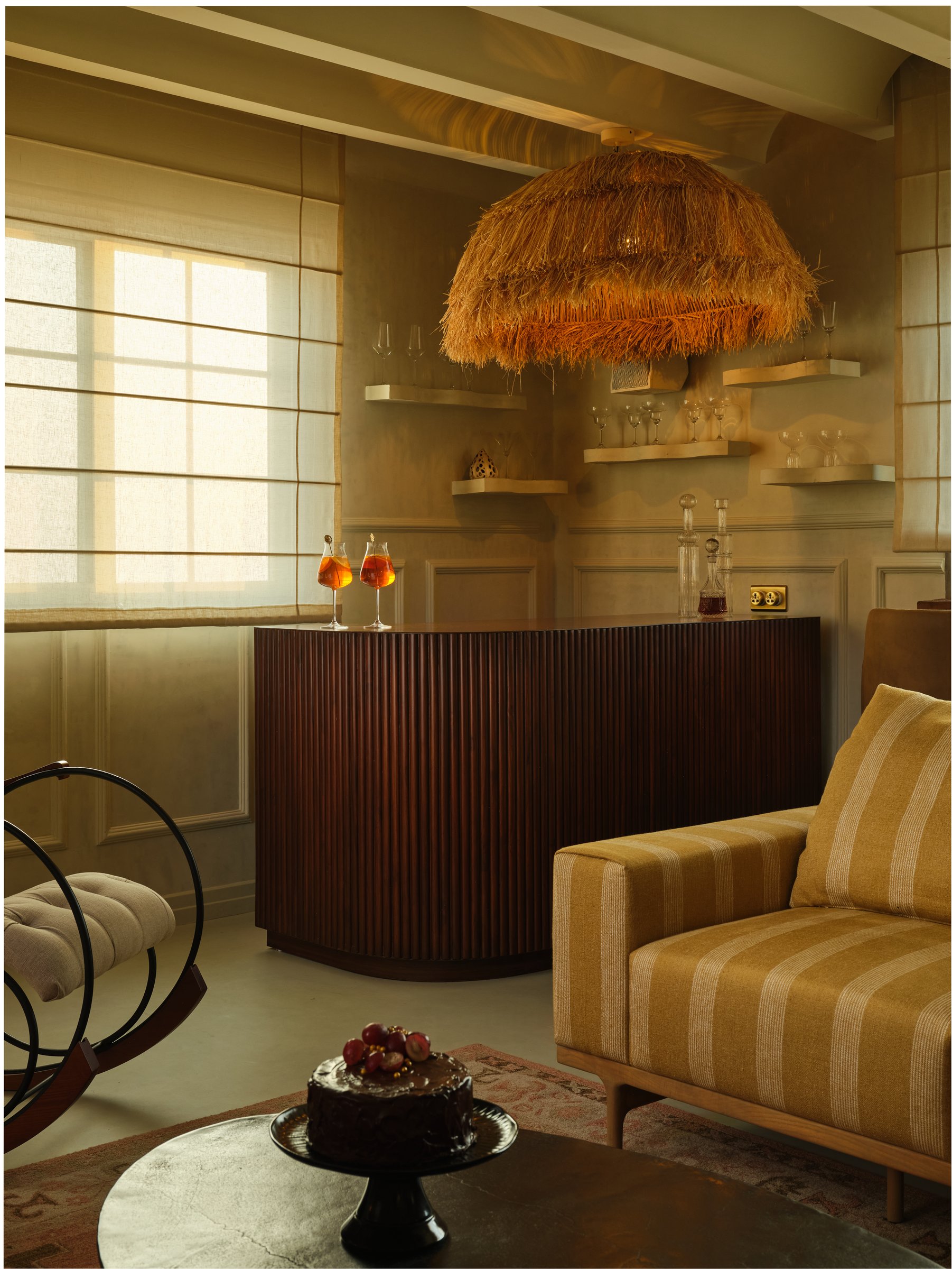 The bar, where a curved fluted counter meets a shaggy raffia pendant in a corner of gilded light