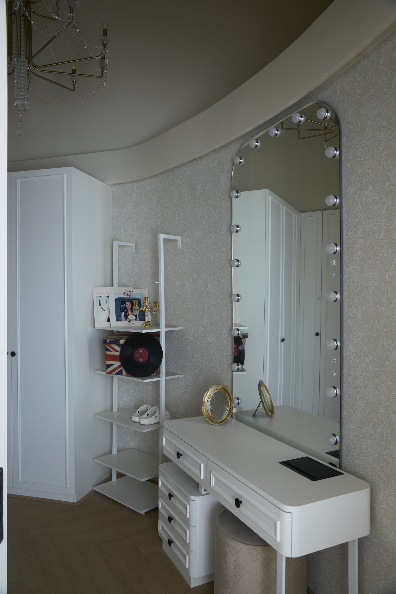 The dressing area, where a bulb-lit mirror sits above a slim vanity beside an open shelving unit