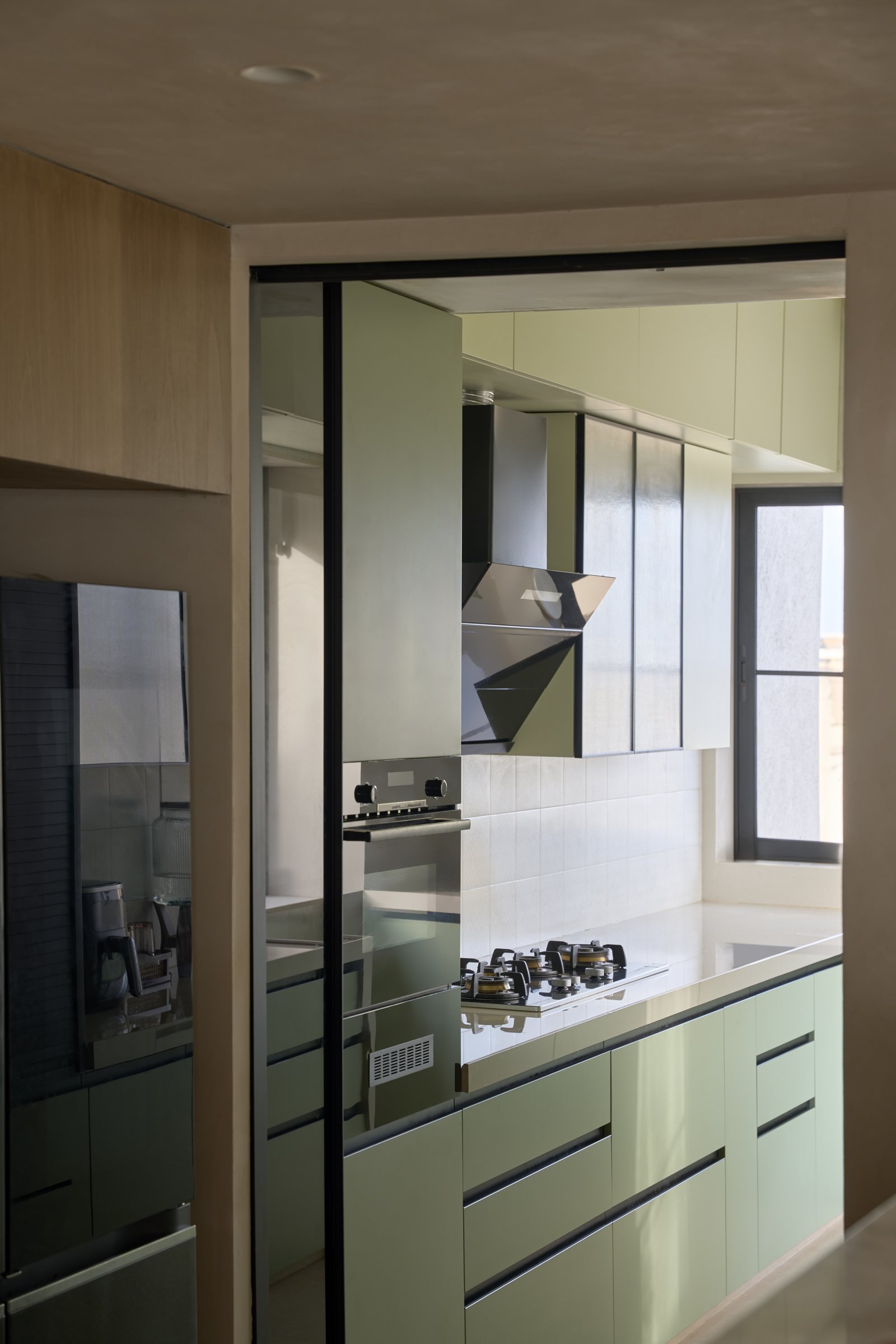 The service kitchen, glimpsed through a sliding partition in soft green cabinetry