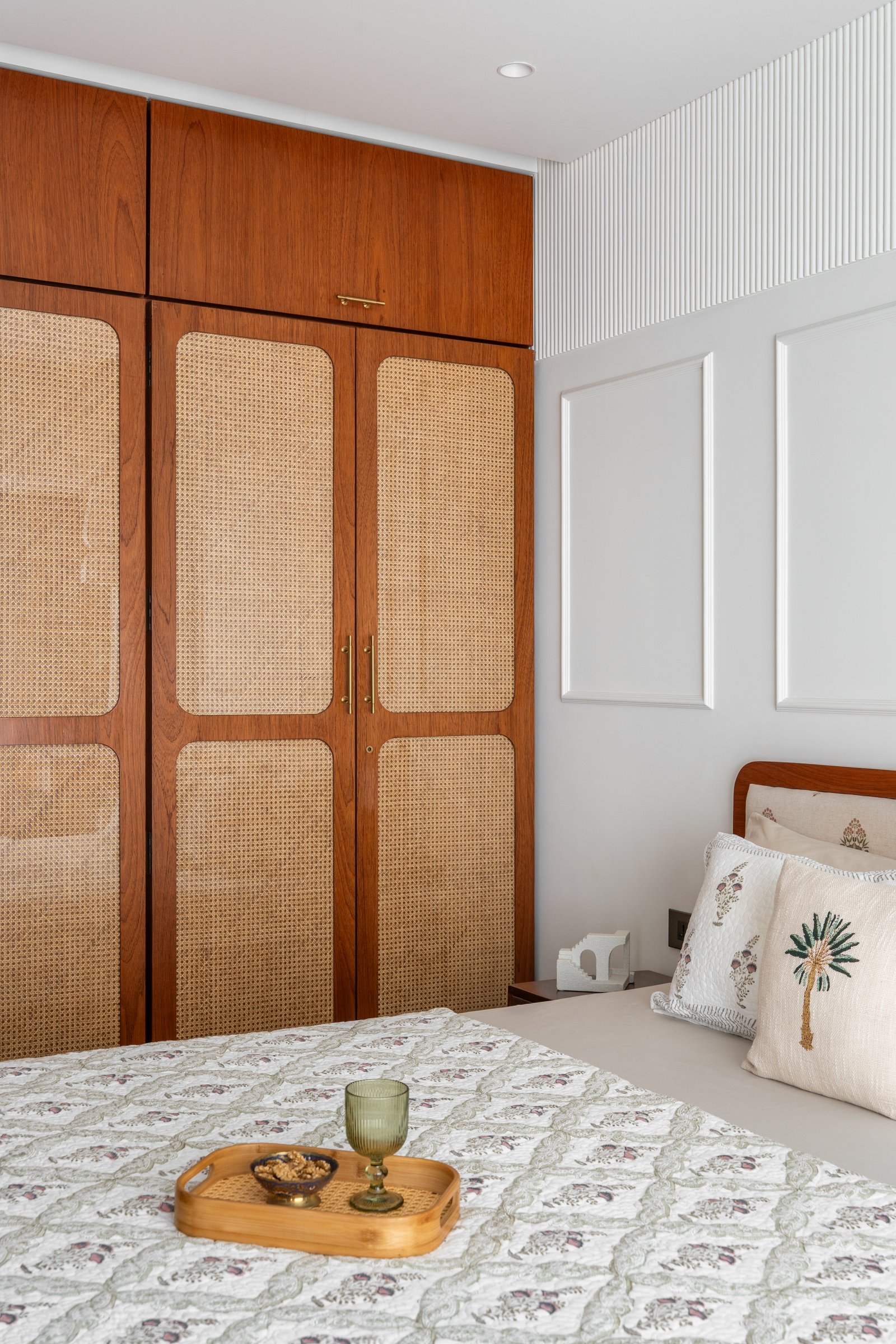 A secondary teak wardrobe with cane-webbed panels sits beside the master bed