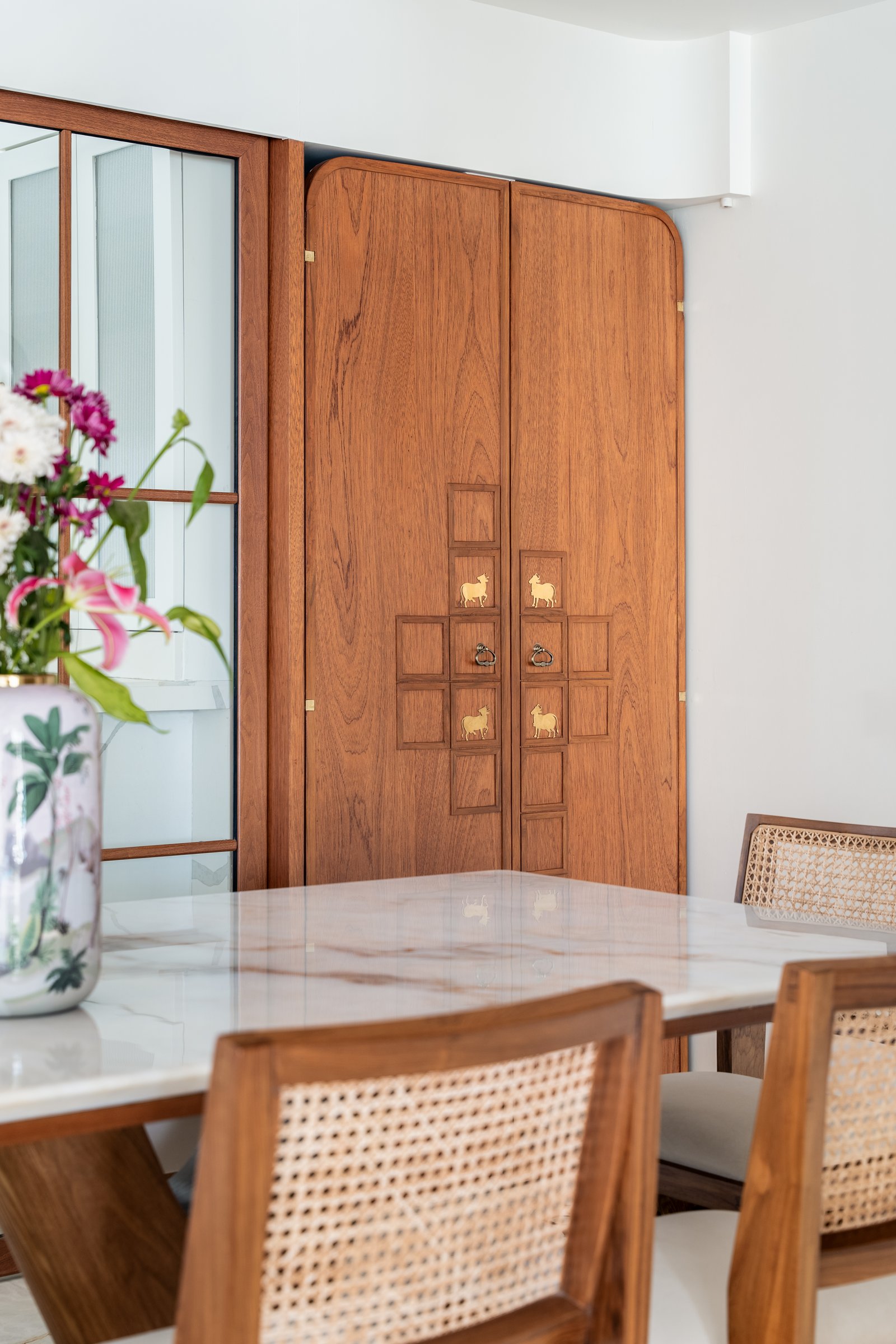 The pooja cabinet closed, its teak doors carrying a brass-inlaid grid punctuated by small cow motifs