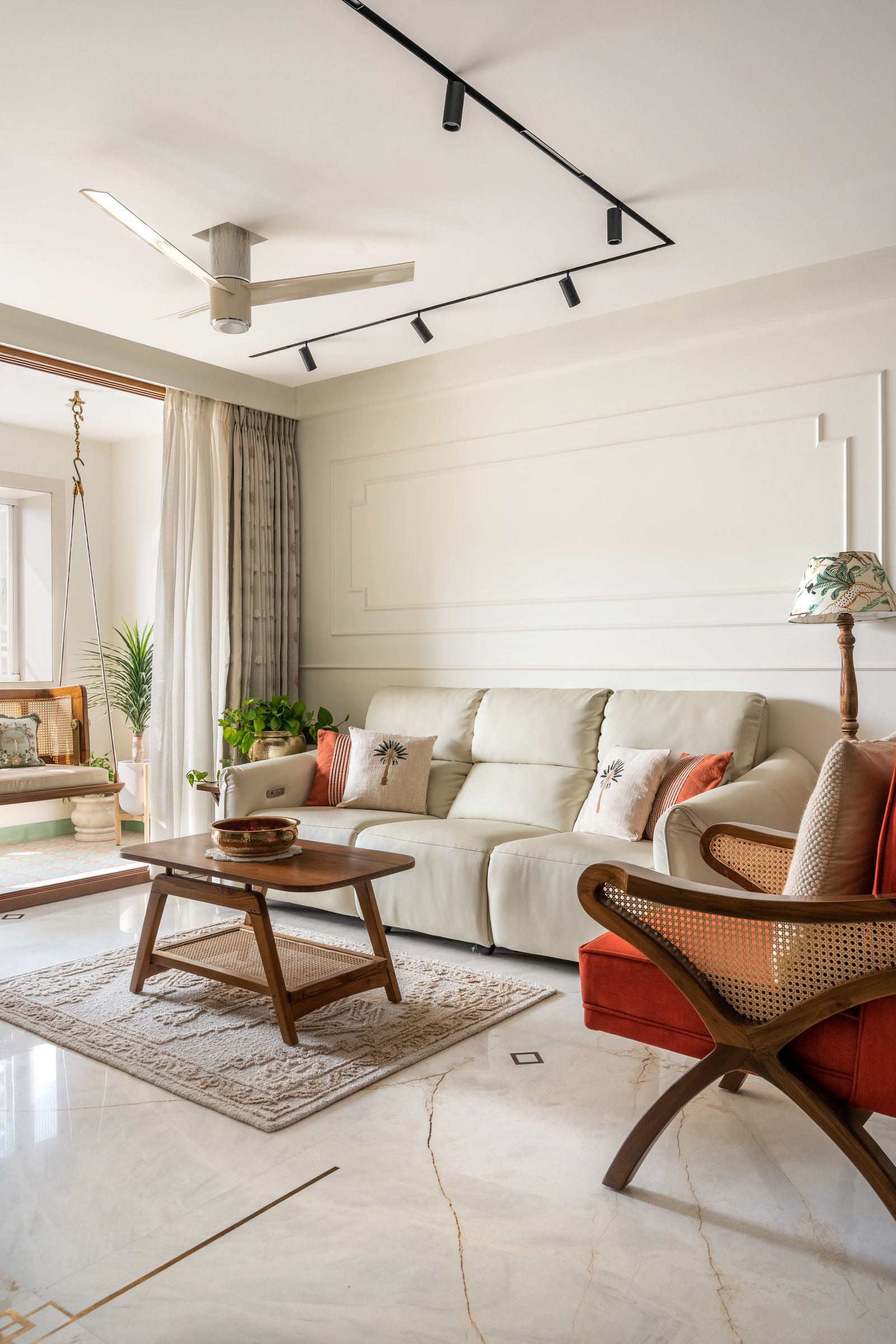 The living room, where a pale leather sofa, a caned rust accent chair, and a low teak coffee table hold a restrained composition against a panelled wall