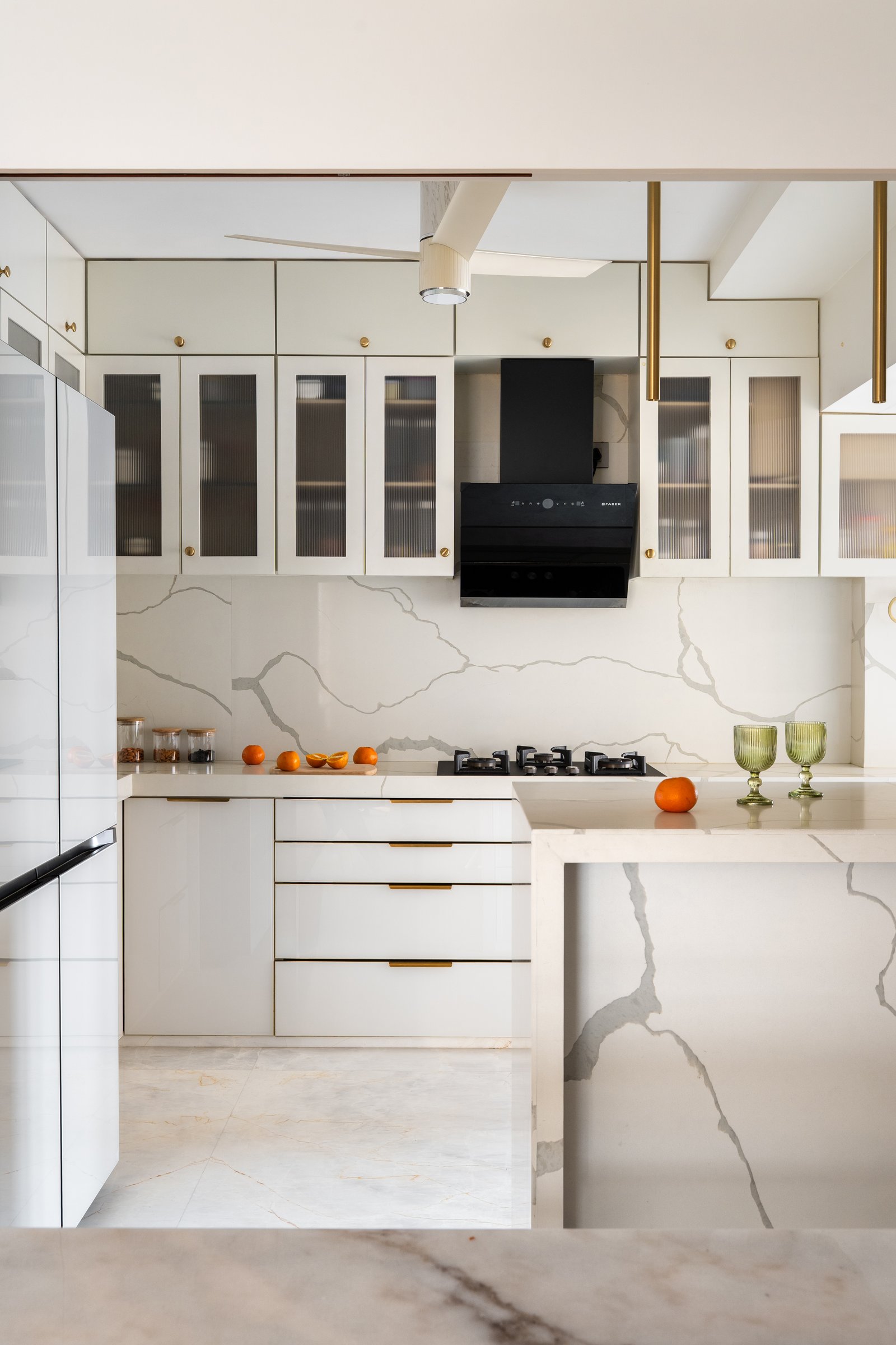 The kitchen, where glossy ivory cabinetry with brass pulls meets a stone-clad wall and waterfall island
