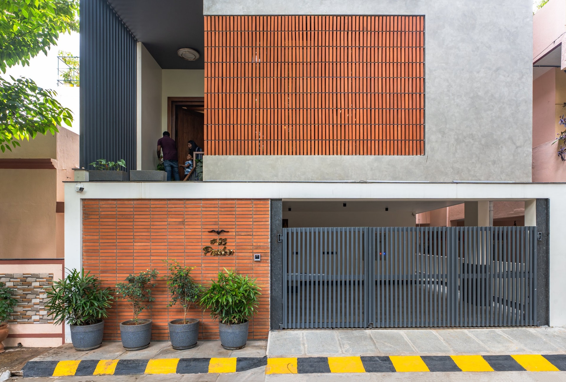 The street-facing elevation, where a ribbed terracotta band at ground level and a perforated brick screen above establish the home's material identity
