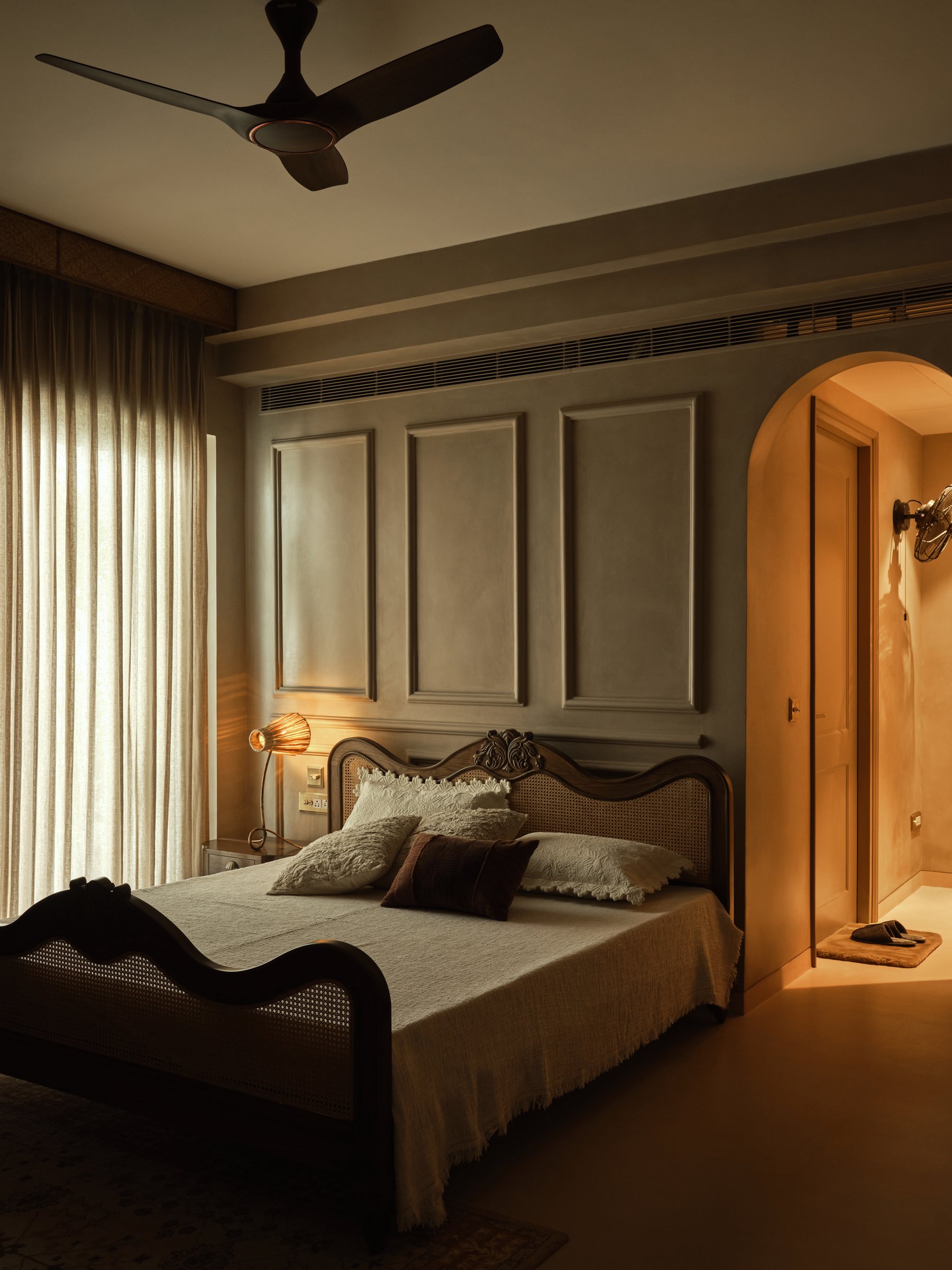 The second guest bedroom, where grey panelling and a cane bed frame register a quieter counterpoint