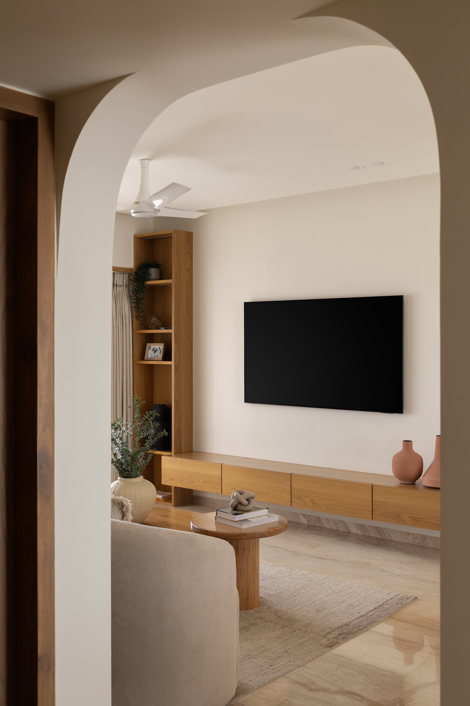 The media wall, composed as a single quiet gesture in warm oak and pale plaster