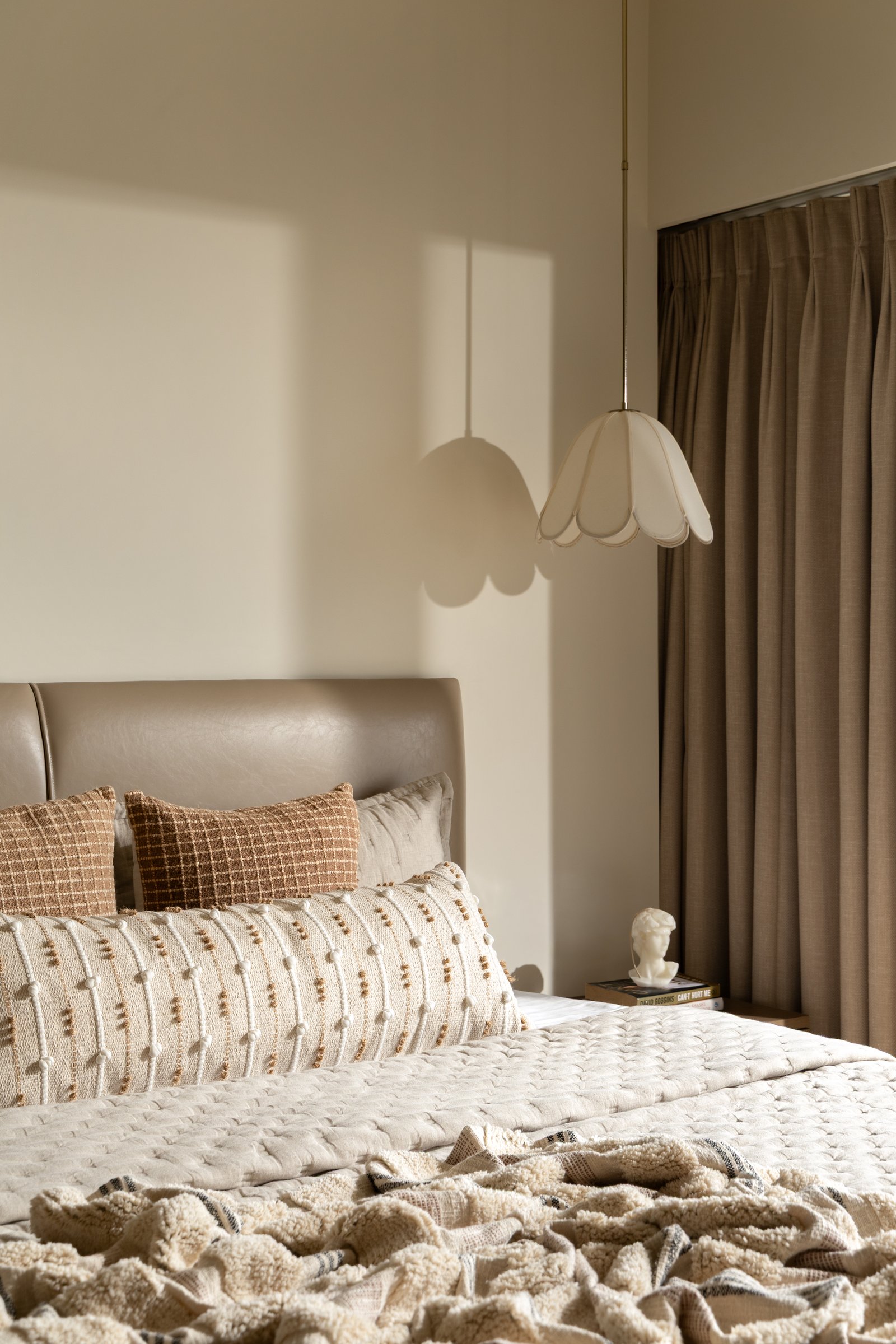 A soft scalloped pendant beside the bed, casting a gentle shadow on the plaster wall