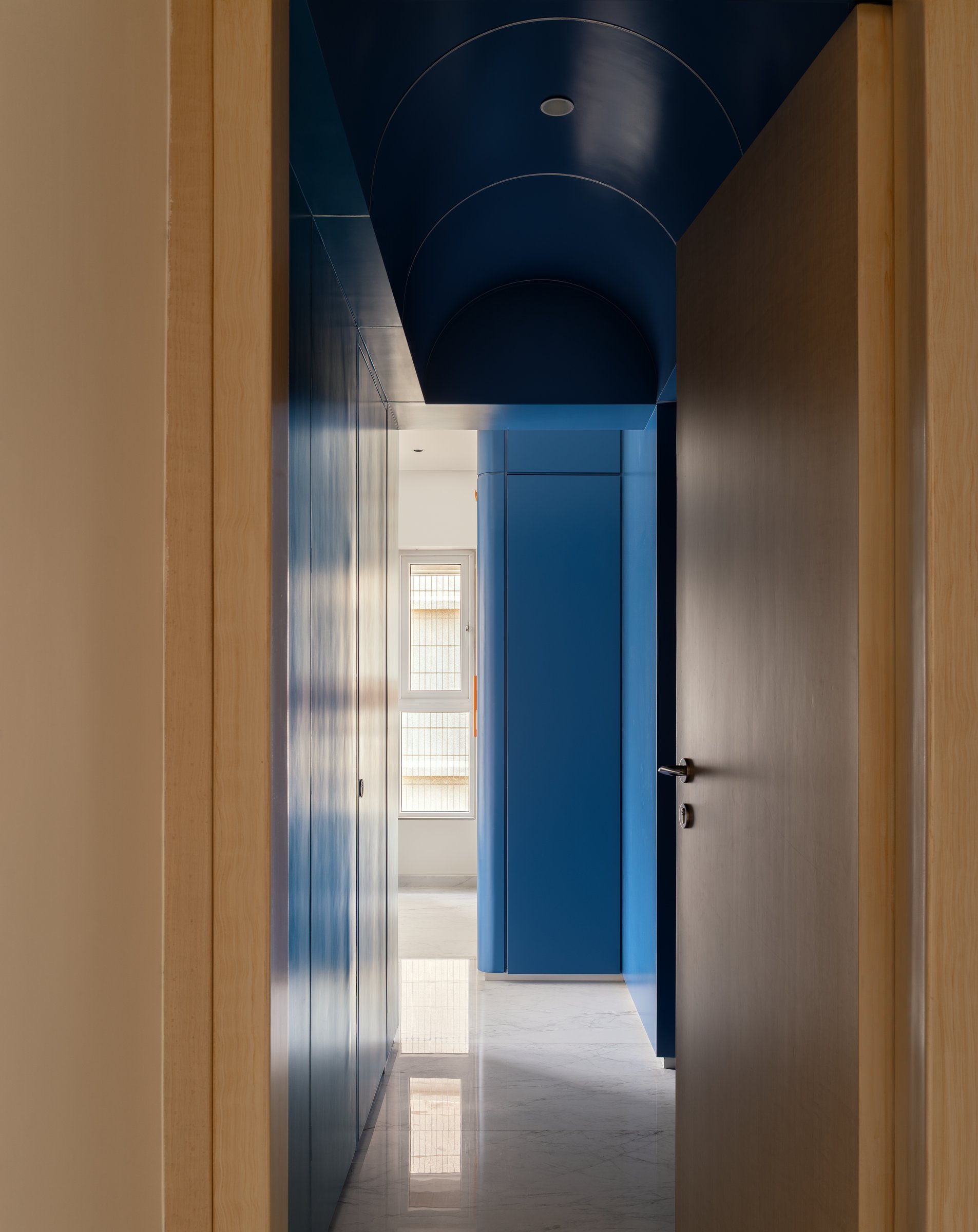 A corridor treated with a deep blue ceiling and matching joinery, contrasting the pale timber door frames that mark its threshold