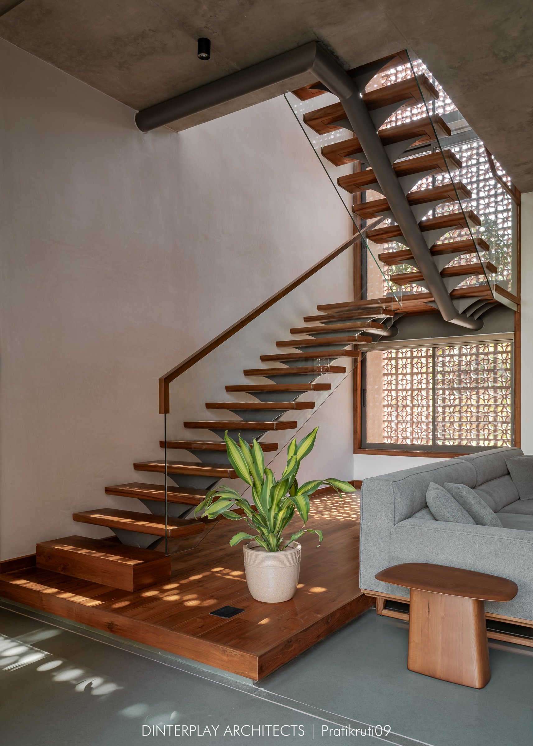 The staircase seen from the base, its cantilevered timber treads framed against a terracotta jaali window