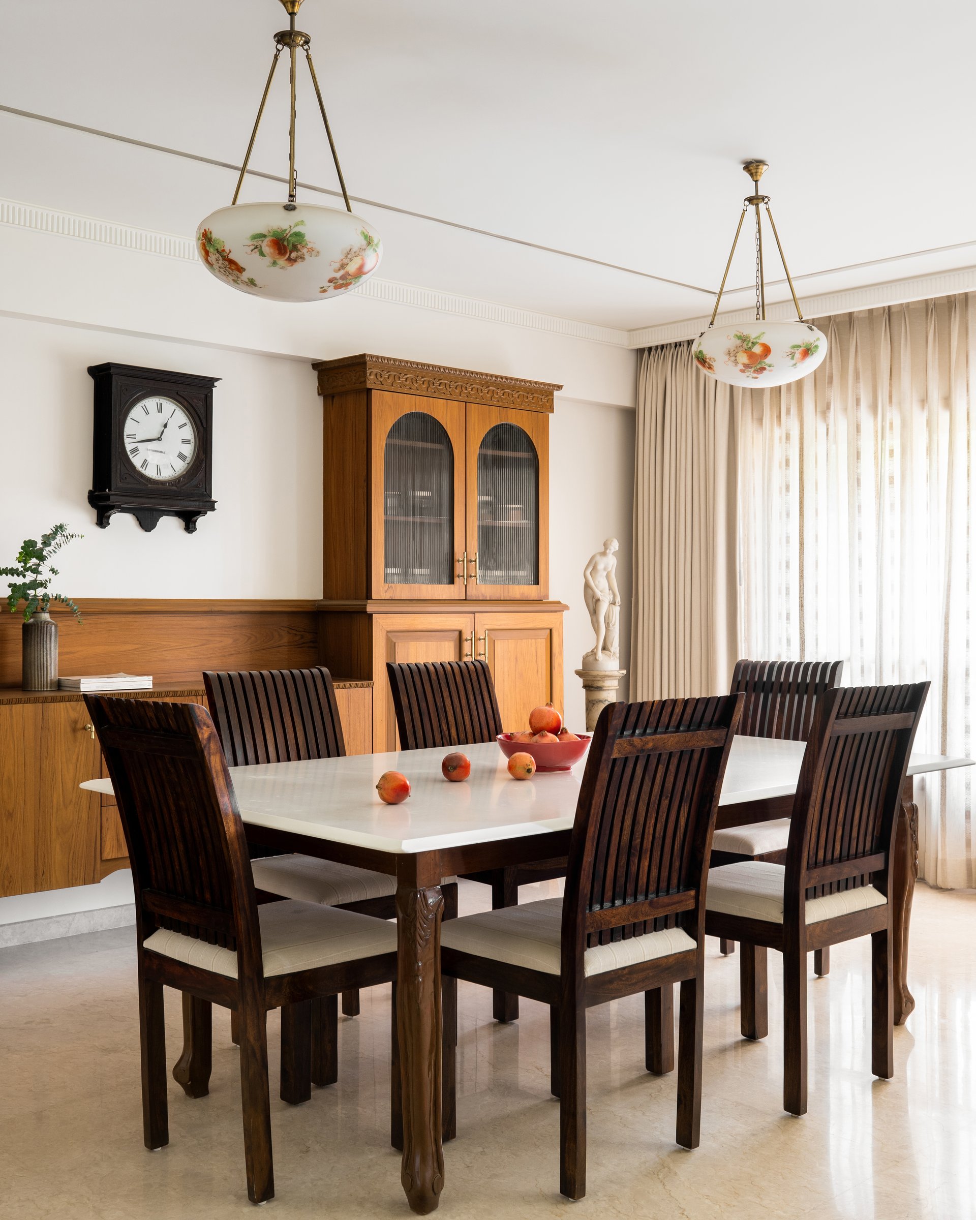 The dining room, anchored by a dark-timber table and a full-height honey-toned sideboard beneath a pair of floral glass pendants