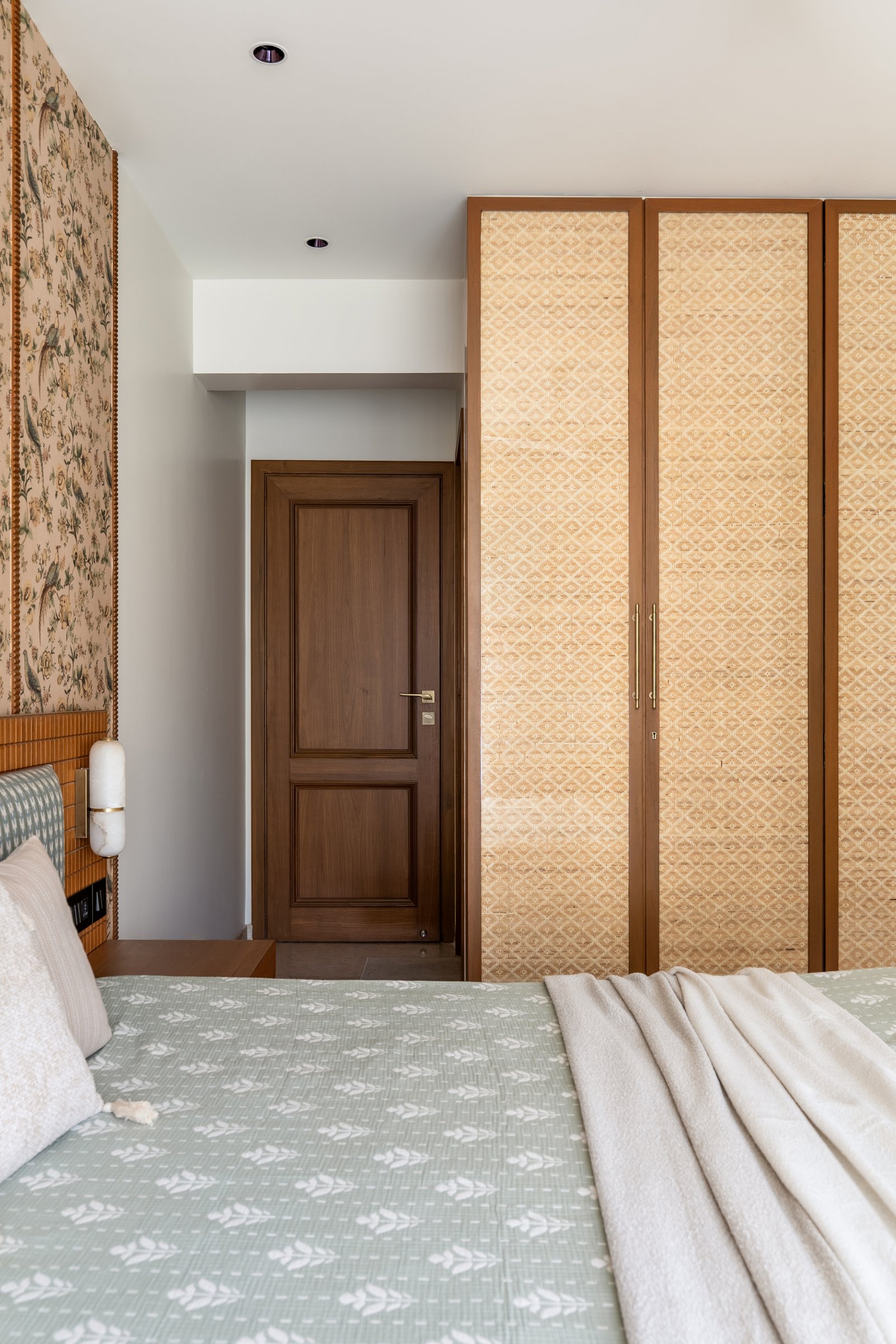 Beyond the bed, woven cane wardrobe fronts framed in warm timber soften the built-in storage