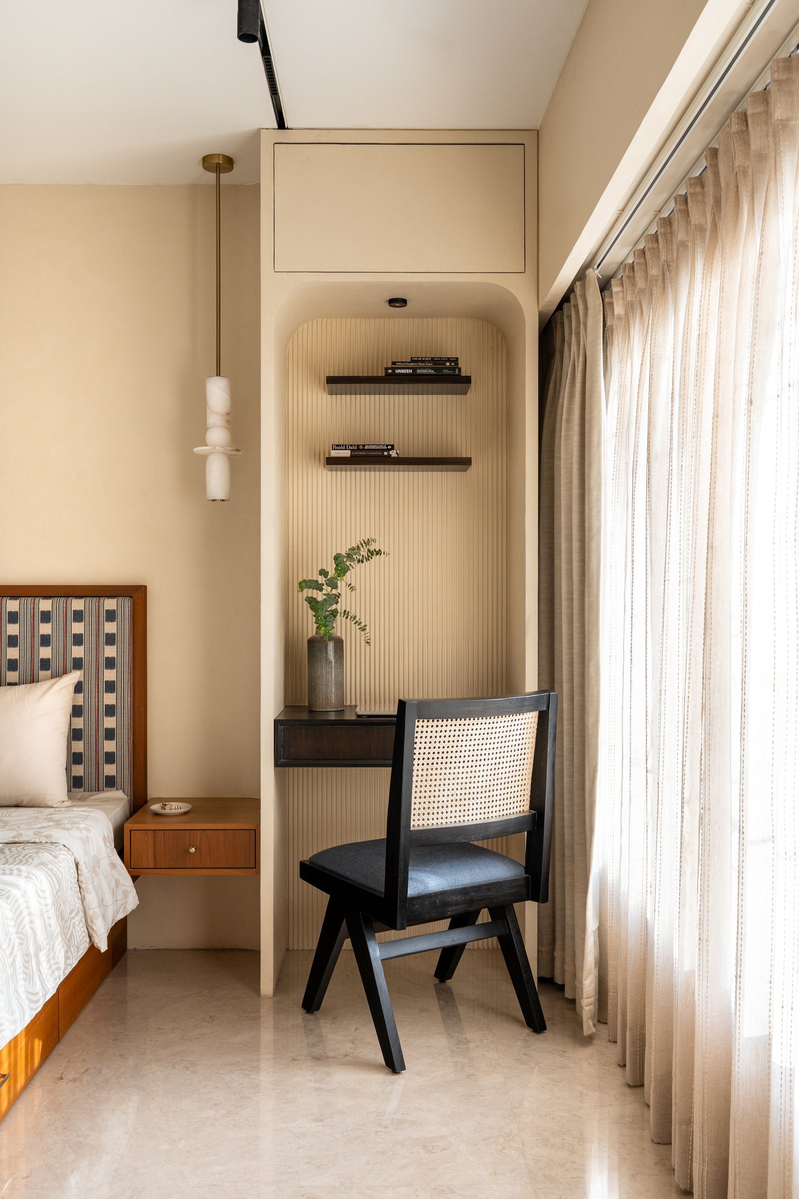 A fluted arched niche opposite the bed holds floating shelves above a slim study desk with a blackened caned chair