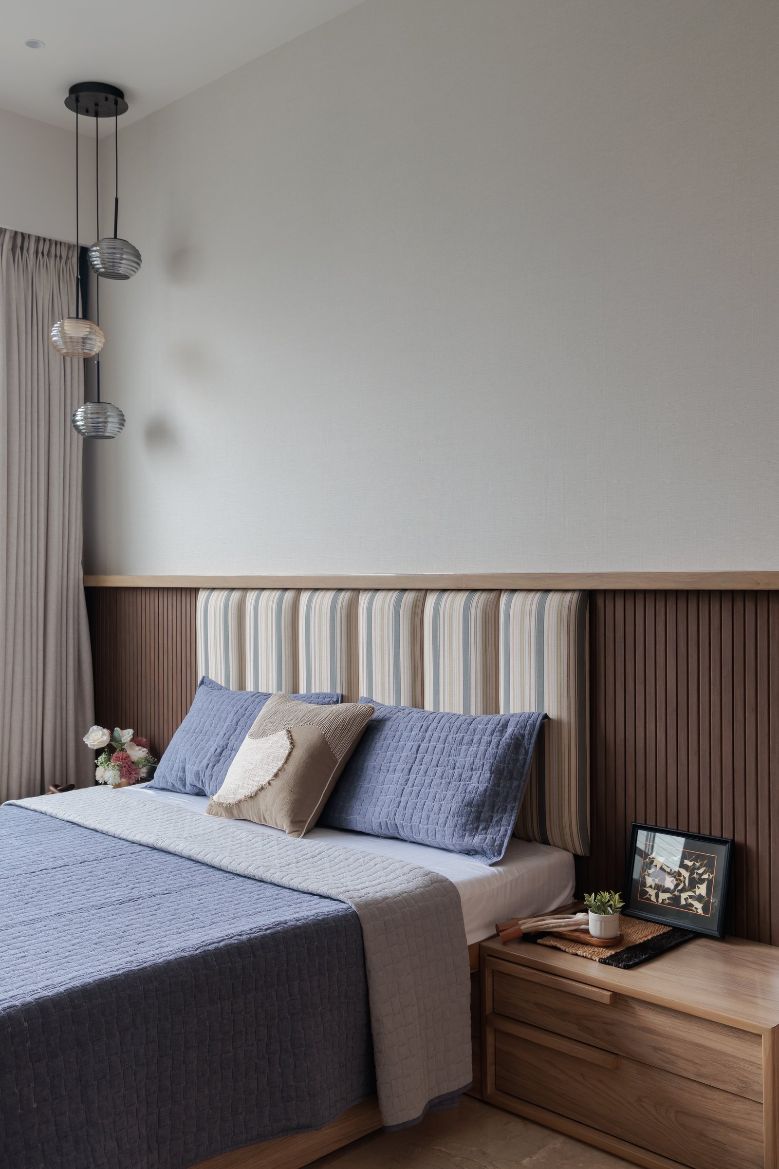 Another bedroom, its striped headboard and fluted timber wainscoting composed against a cluster of pendant lights