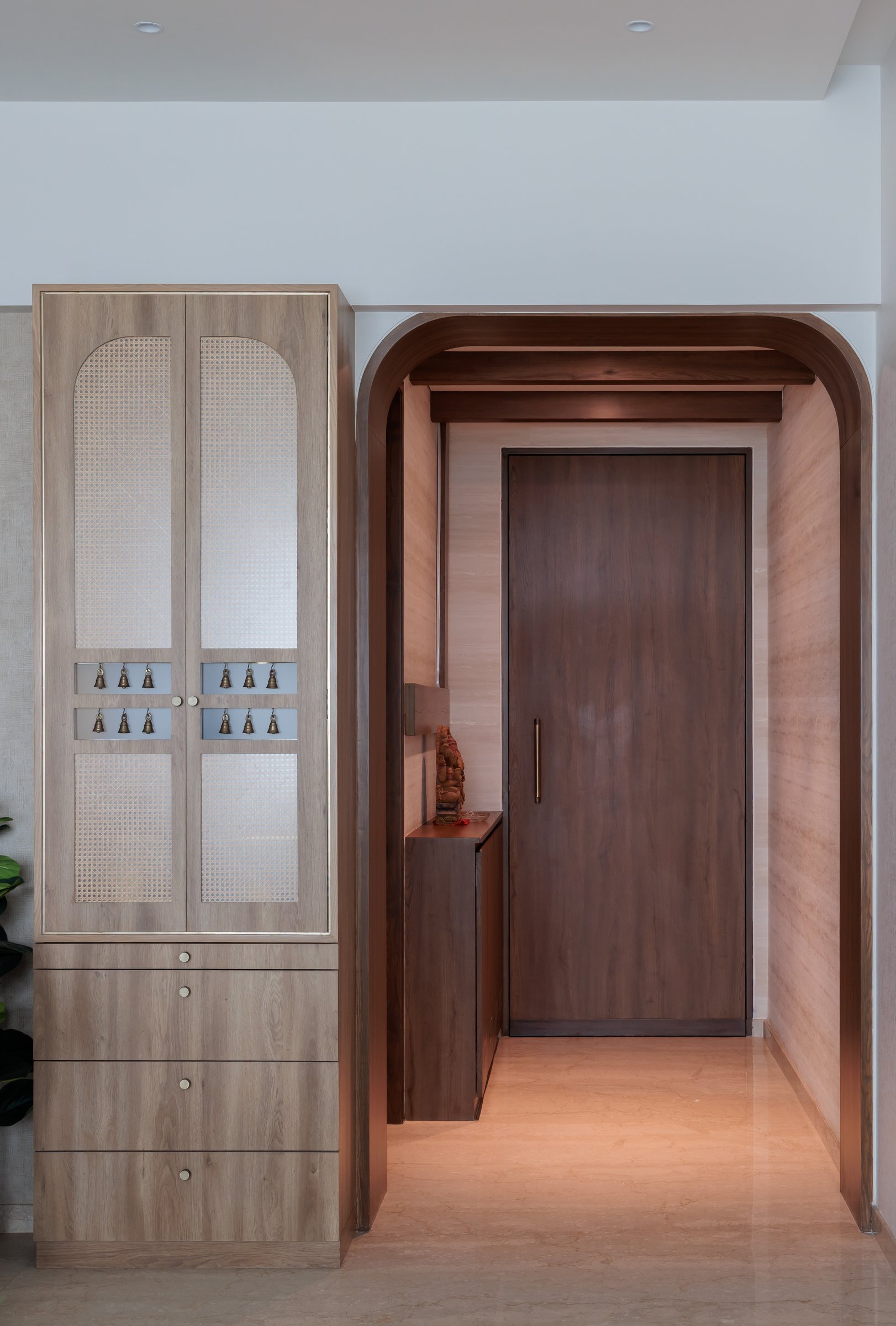 The entry sequence, where a caned ritual cabinet meets a rounded timber archway framing the main door