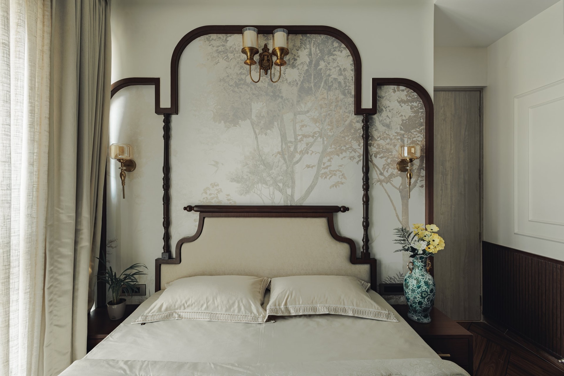 The master bedroom, where a curved walnut headboard and botanical mural are framed by turned spindles and brass sconces
