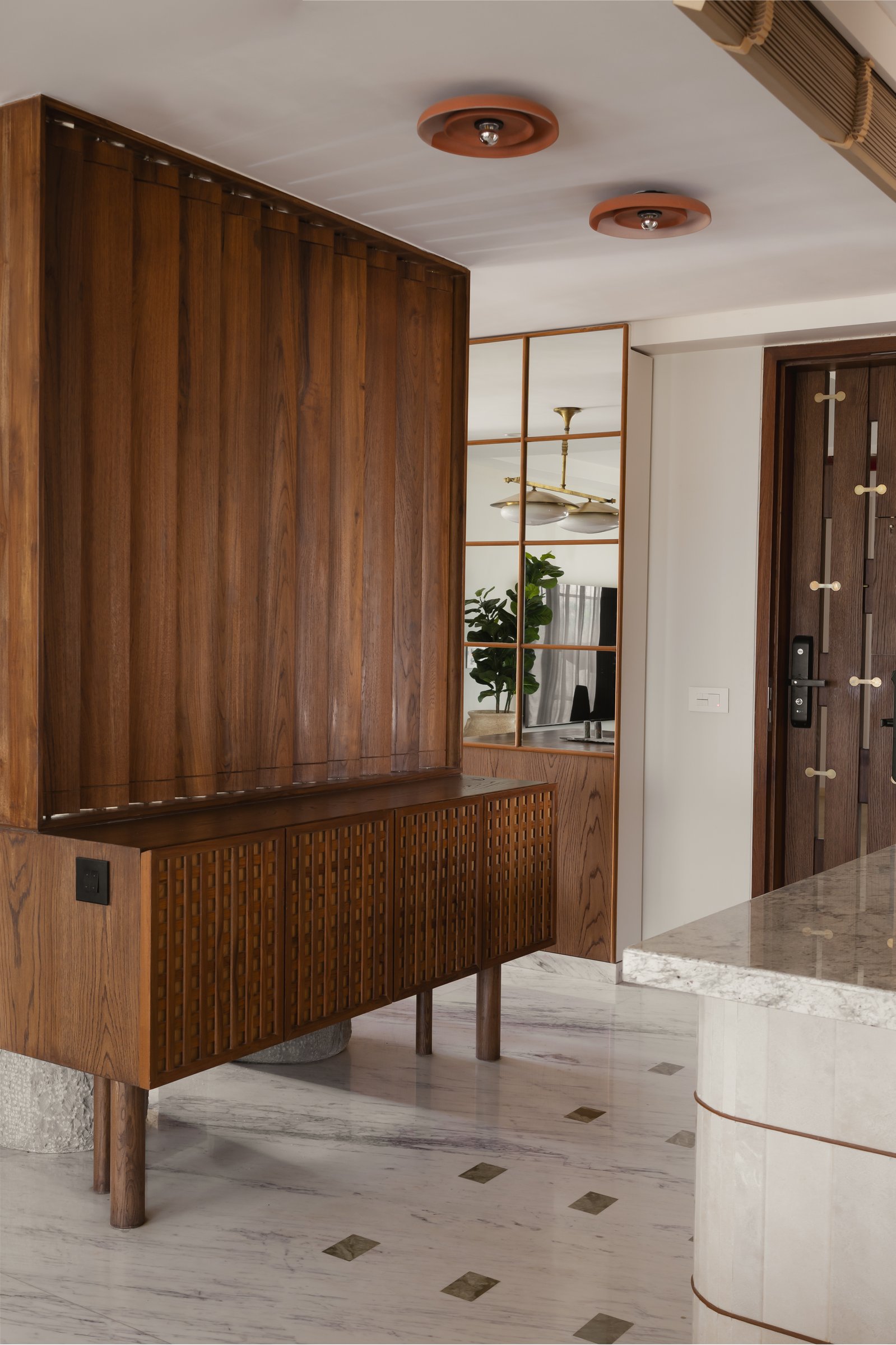 The foyer console in teak, backed by a fluted panel and a gridded mirror that expands the sightline into the living room